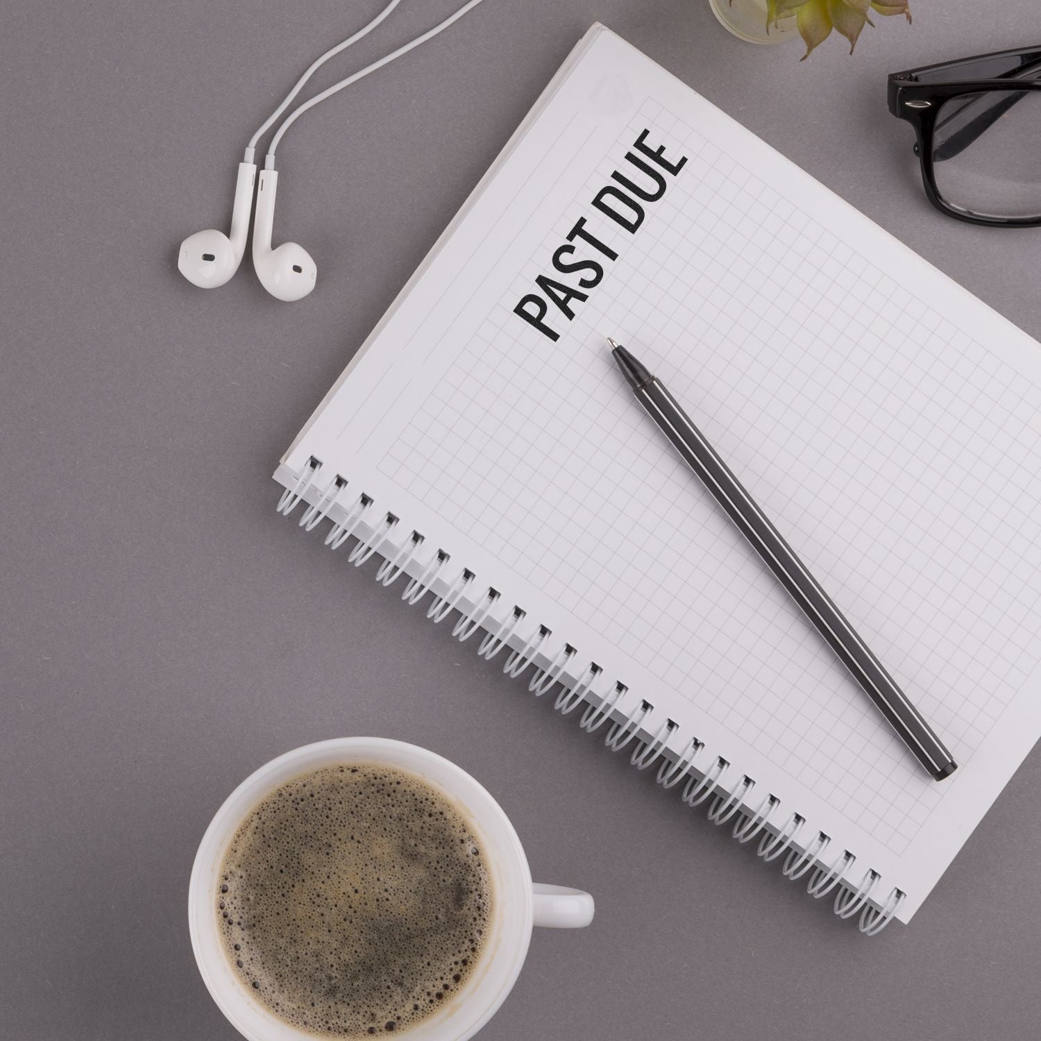 Notebook stamped with PAST DUE using Large Narrow Bold Past Due Rubber Stamp, alongside a pen, coffee cup, glasses, and earphones on a desk.