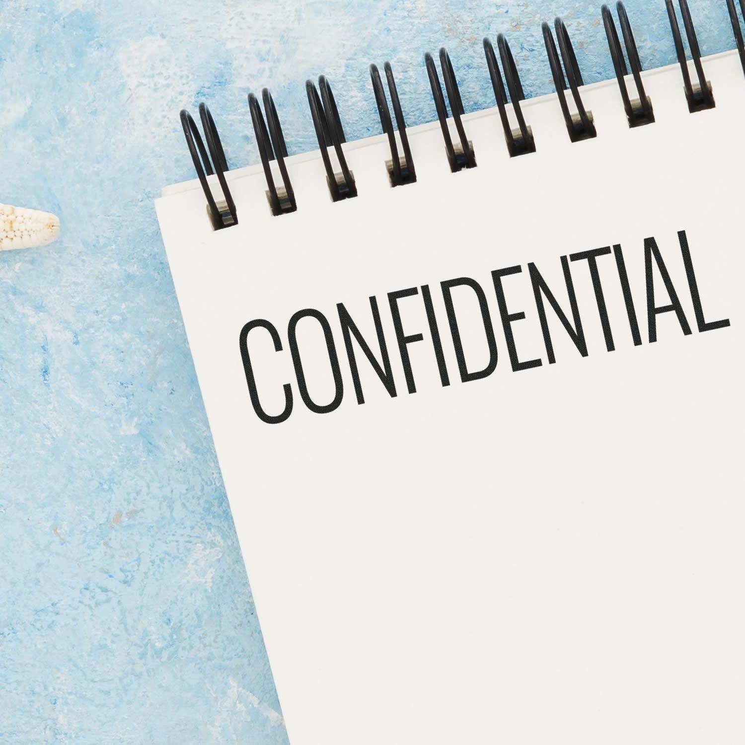 Large Self Inking Narrow Font Confidential Stamp marking CONFIDENTIAL on a white notepad with a blue background.