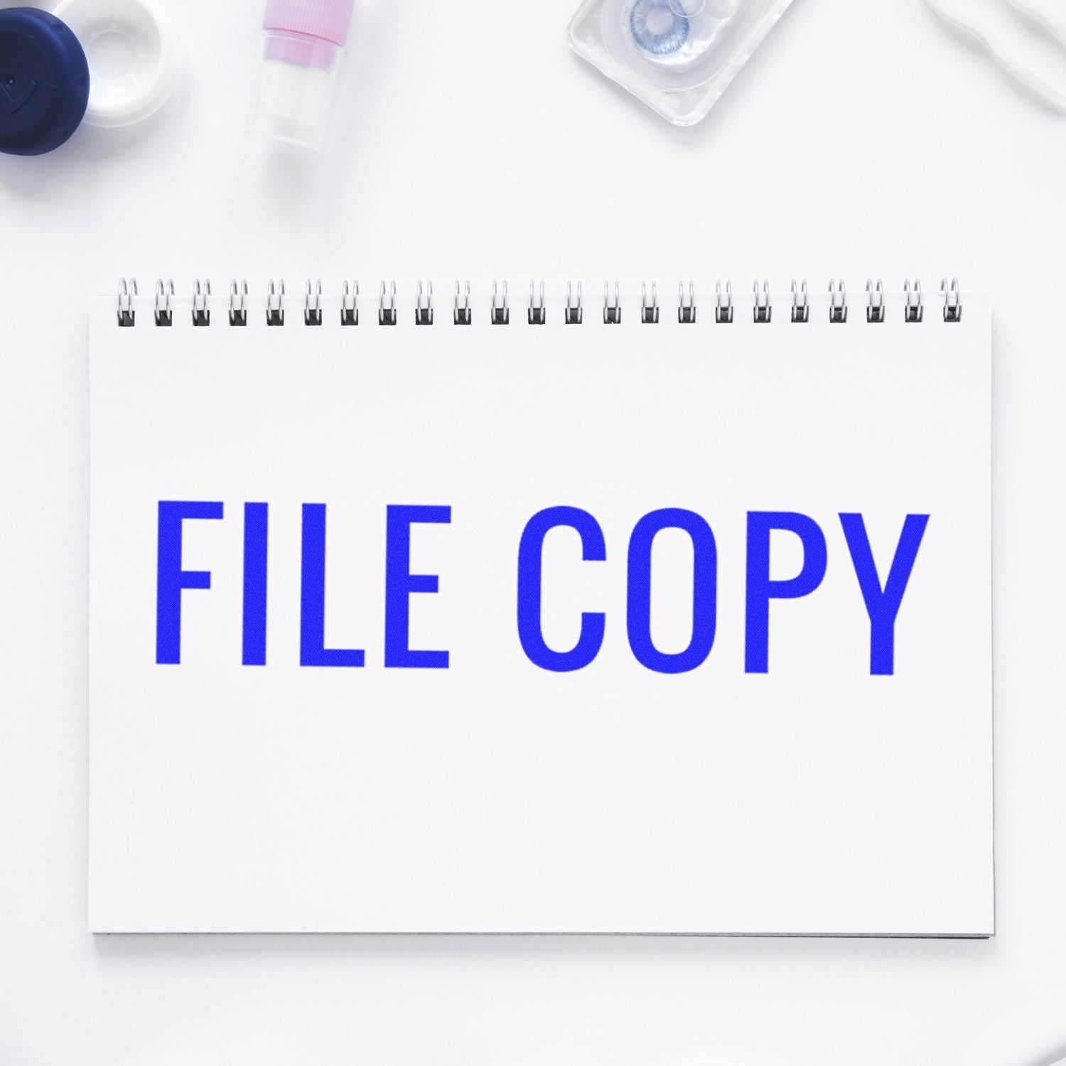 Large Pre-Inked Narrow Font File Copy Stamp in blue ink on a white spiral notebook, surrounded by office supplies.