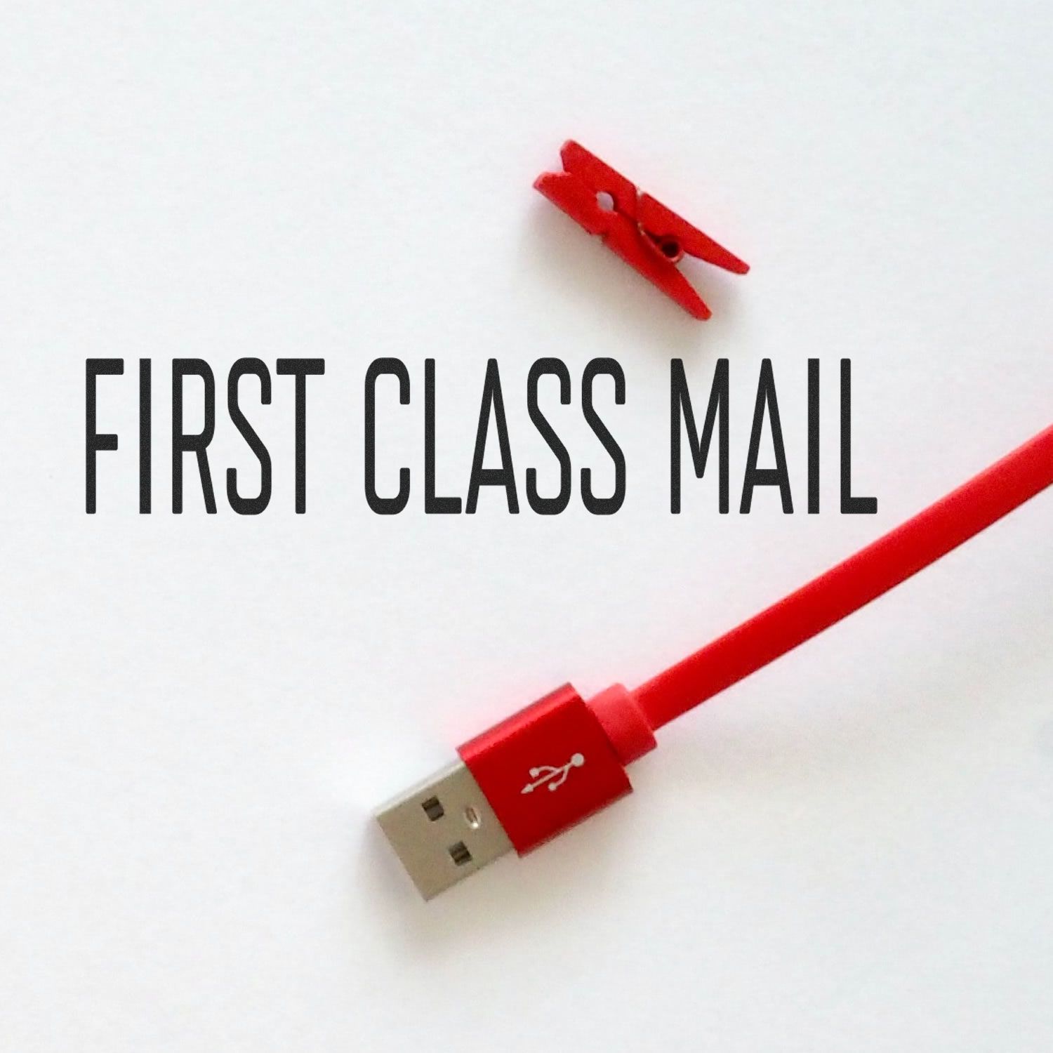 Large Narrow Font First Class Mail Rubber Stamp in use, with a red USB cable and a small red clothespin on a white background.