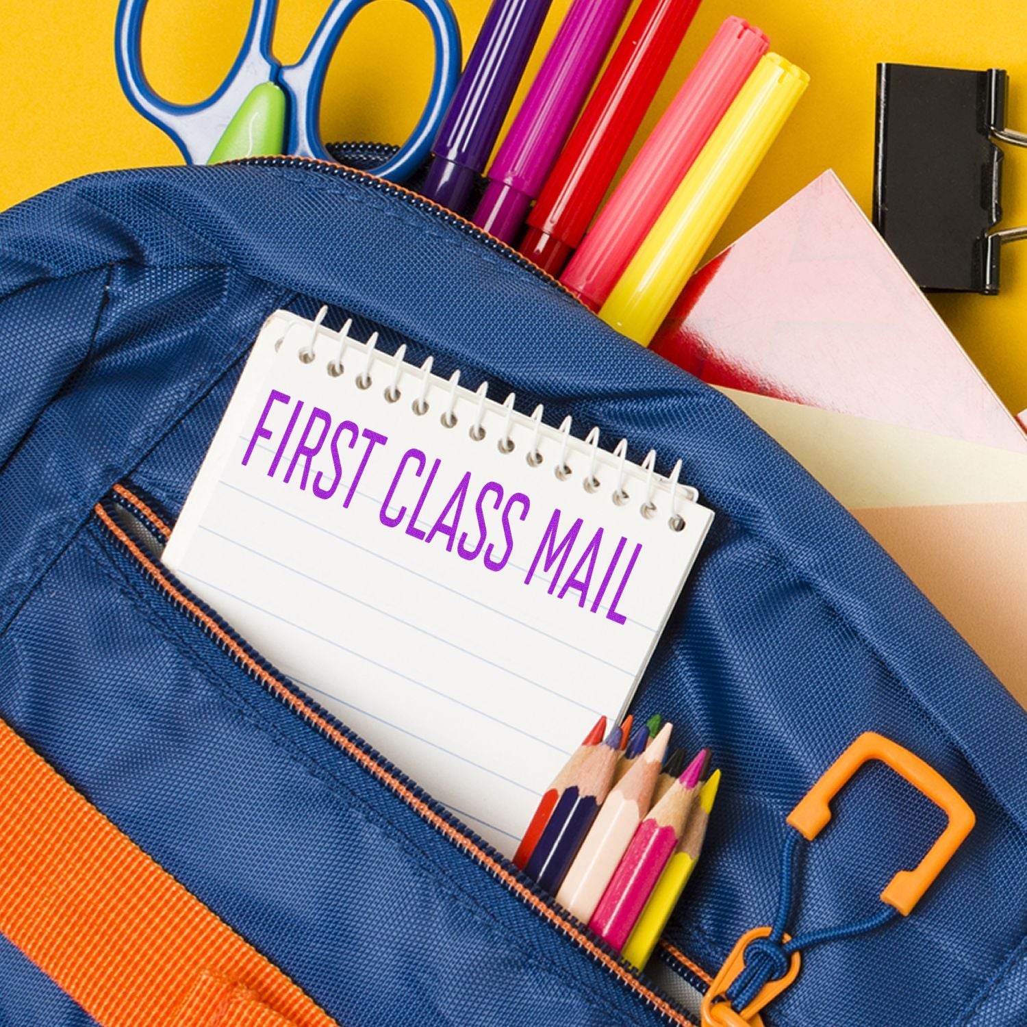 A blue backpack with colored pencils, markers, scissors, and a notepad stamped with FIRST CLASS MAIL using the Large Self Inking Narrow Font First Class Mail Stamp.