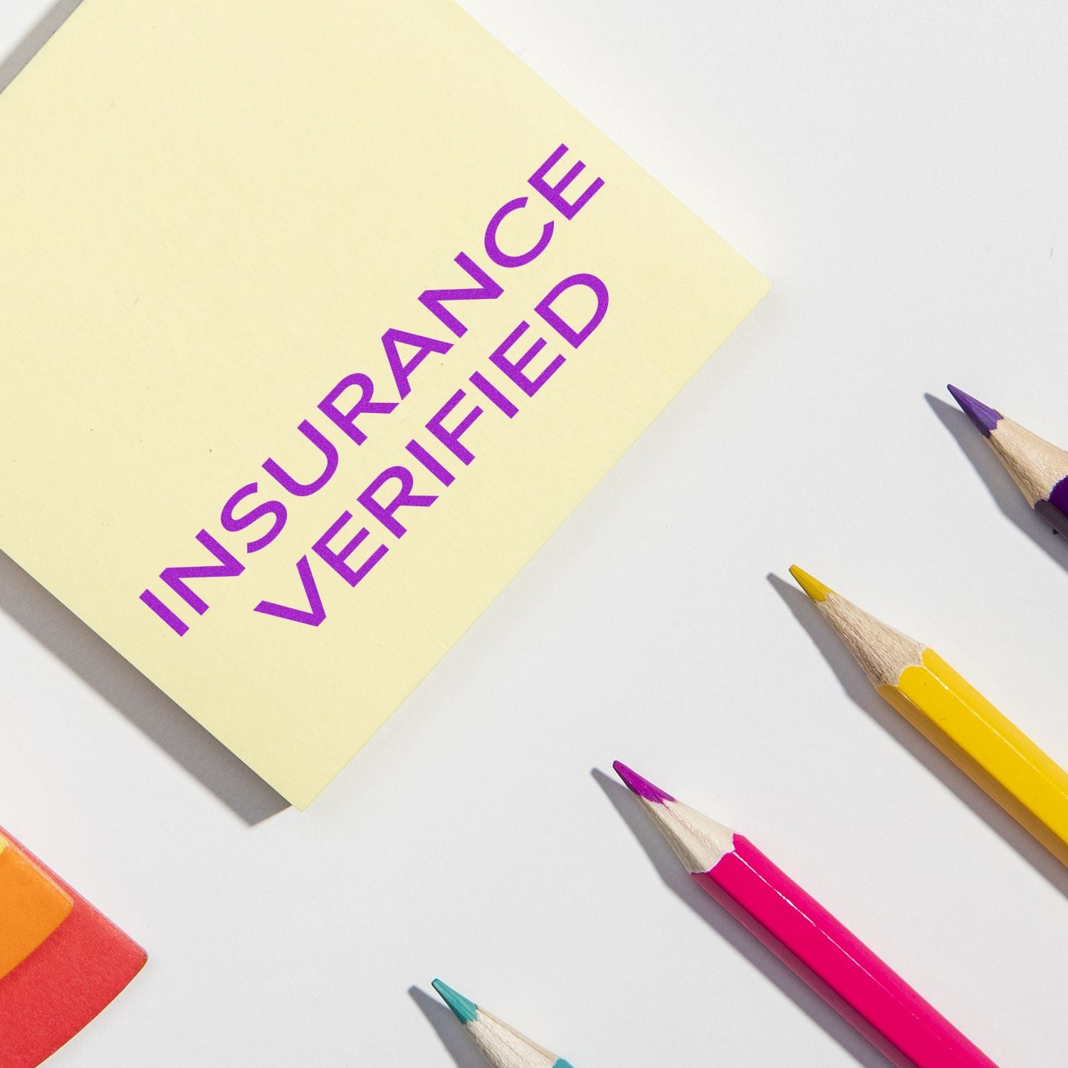 Yellow sticky note stamped with INSURANCE VERIFIED using the Large Pre-Inked Narrow Font Insurance Verified Stamp, surrounded by colorful pencils.