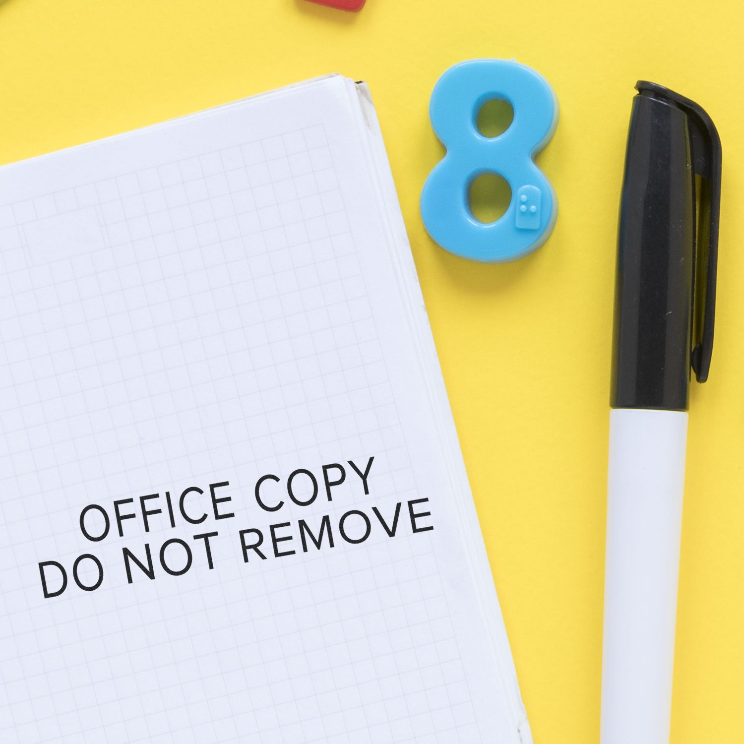 Notebook stamped with OFFICE COPY DO NOT REMOVE using the Large Narrow Font Office Copy Do Not Remove Rubber Stamp, next to a pen and blue number 8.