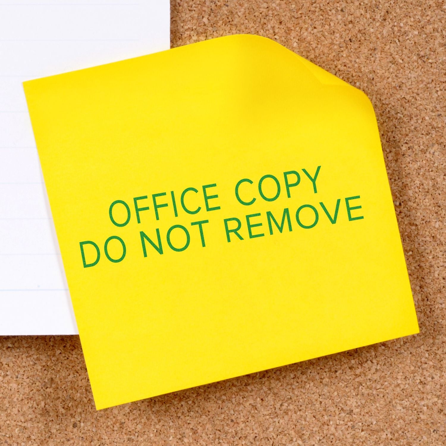 Slim Pre-Inked Narrow Font Office Copy Do Not Remove Stamp on a yellow sticky note attached to a corkboard.