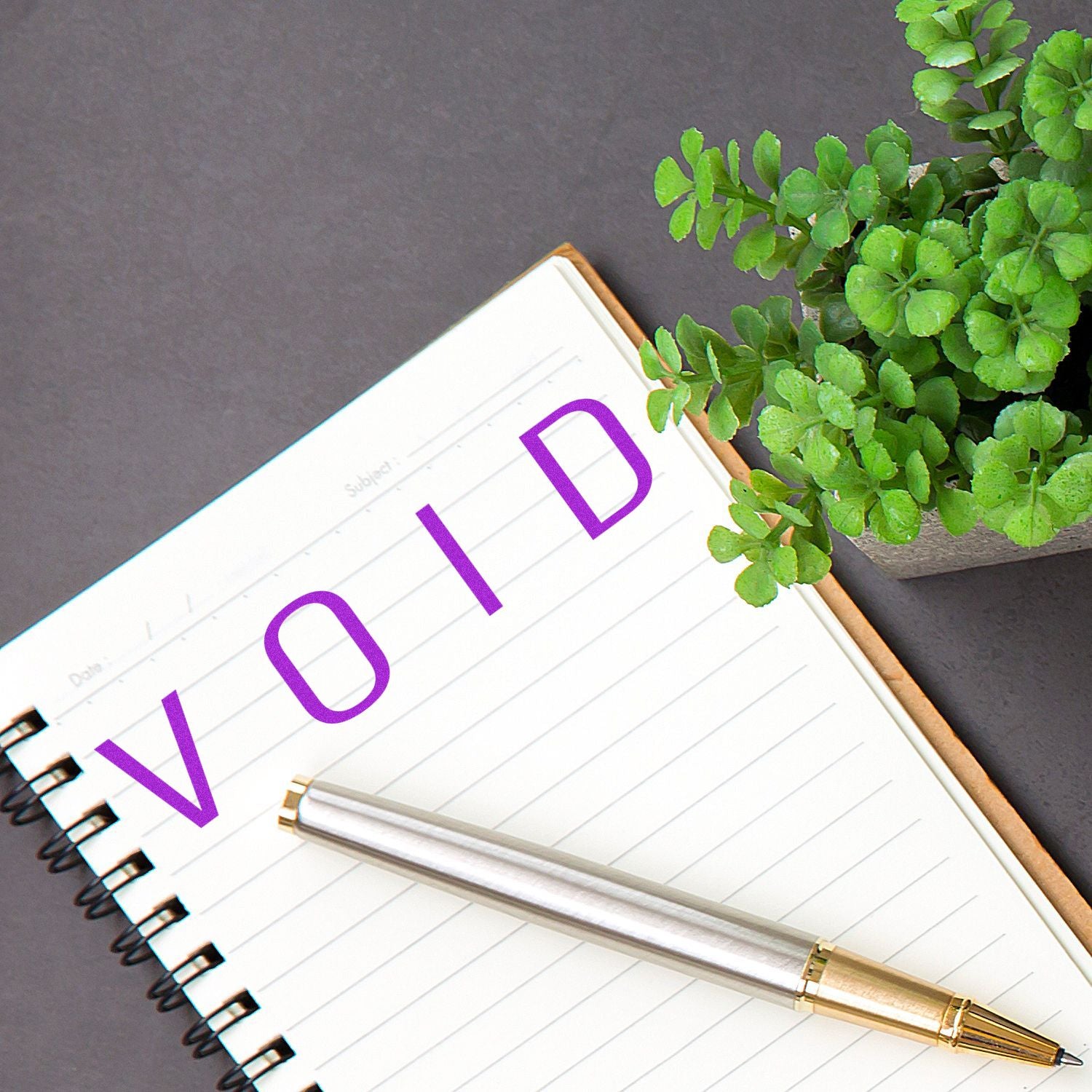 Large Pre-Inked Narrow Void Stamp marking VOID in purple ink on a lined notebook, with a pen and a potted plant nearby.