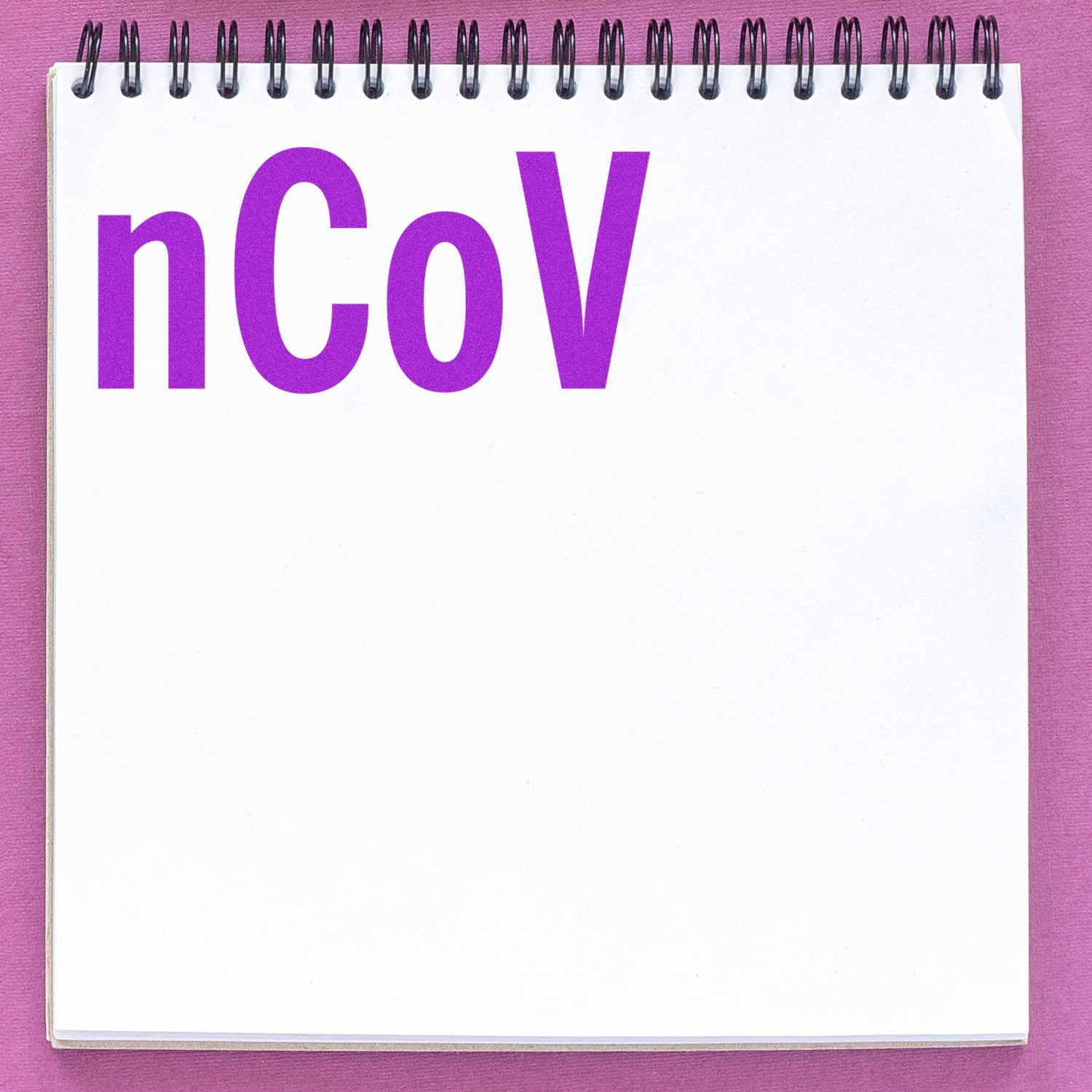 A Large Pre-Inked nCov Stamp imprint in bold purple letters on a white notepad with a spiral binding, placed on a pink surface.