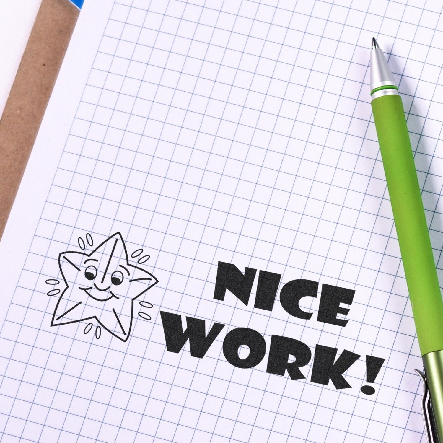 Nice Work Rubber Stamp on graph paper with a green pen beside it, featuring a smiling star illustration.