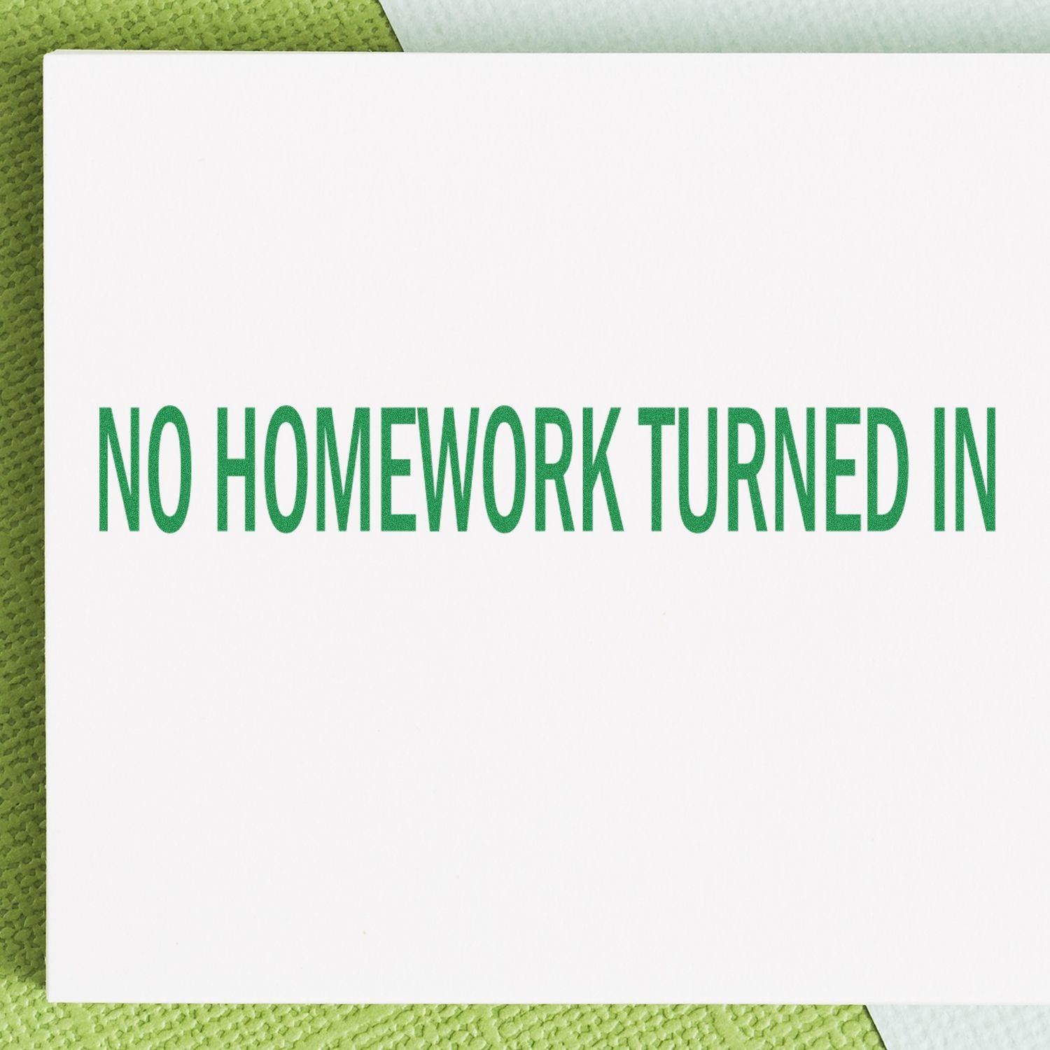 Large Pre-Inked No Homework Turned In Stamp in green ink on white paper, placed on a green textured surface.