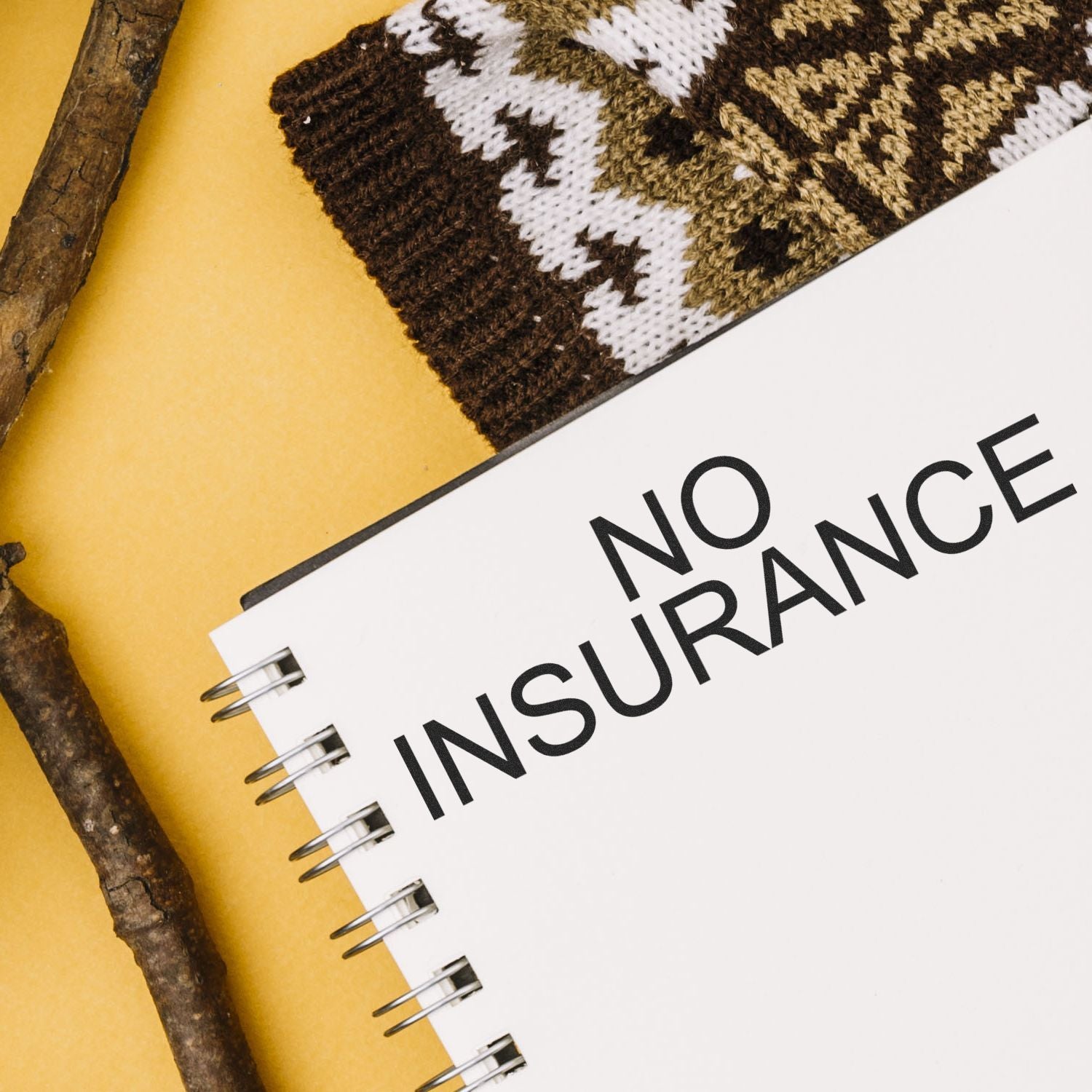 Large No Insurance Rubber Stamp imprint on a white spiral notebook, with a patterned fabric and wooden sticks in the background.