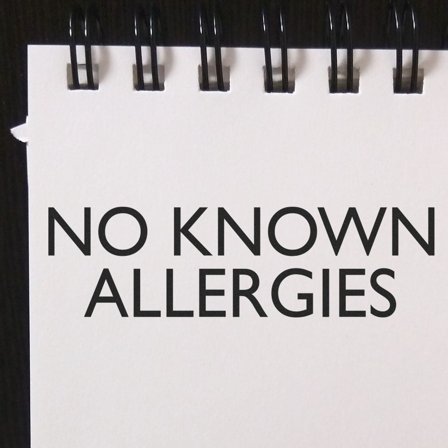 Slim Pre-Inked No Known Allergies Stamp used on a white notepad with black spiral binding.