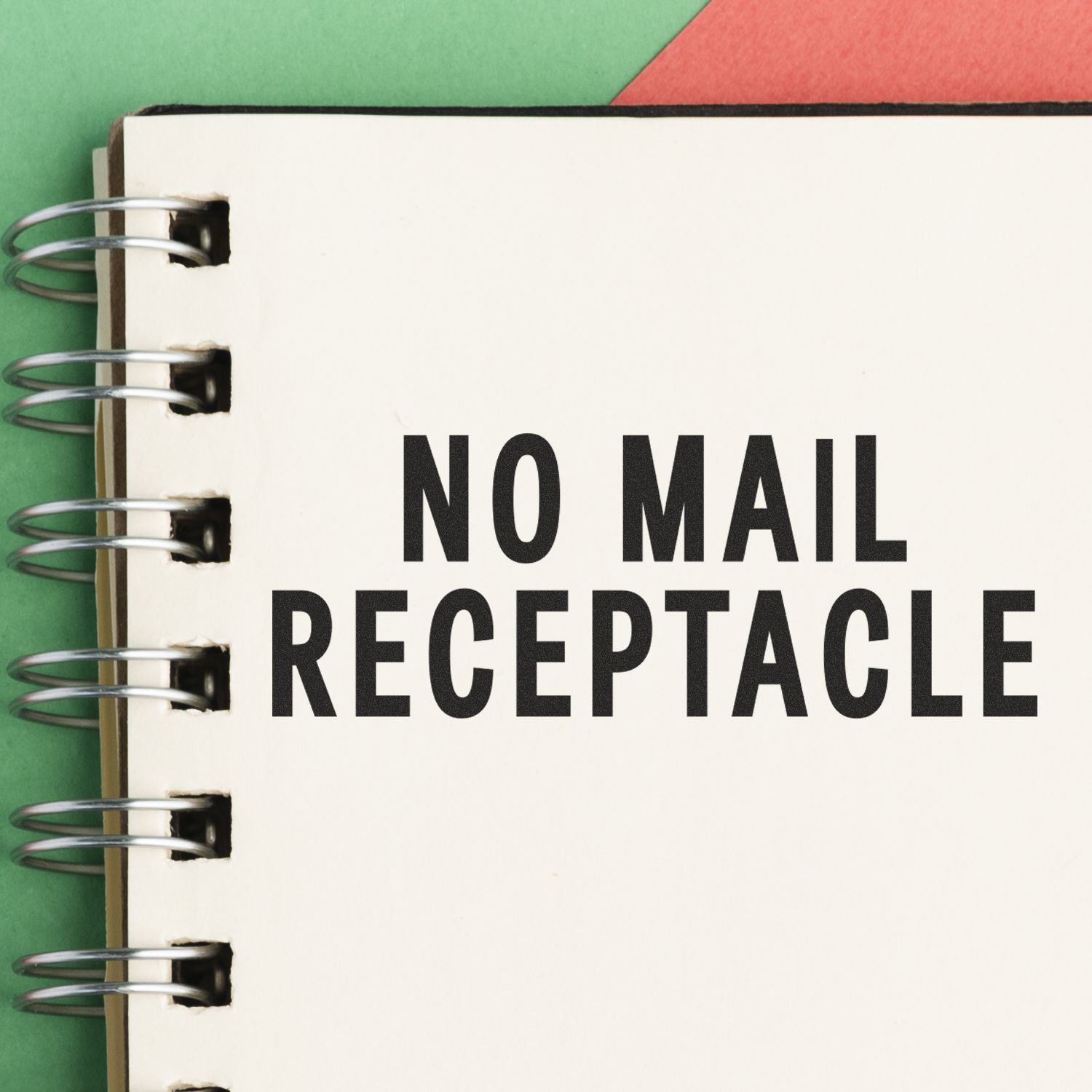 No Mail Receptacle rubber stamp impression on a spiral-bound notebook with a green and red background.