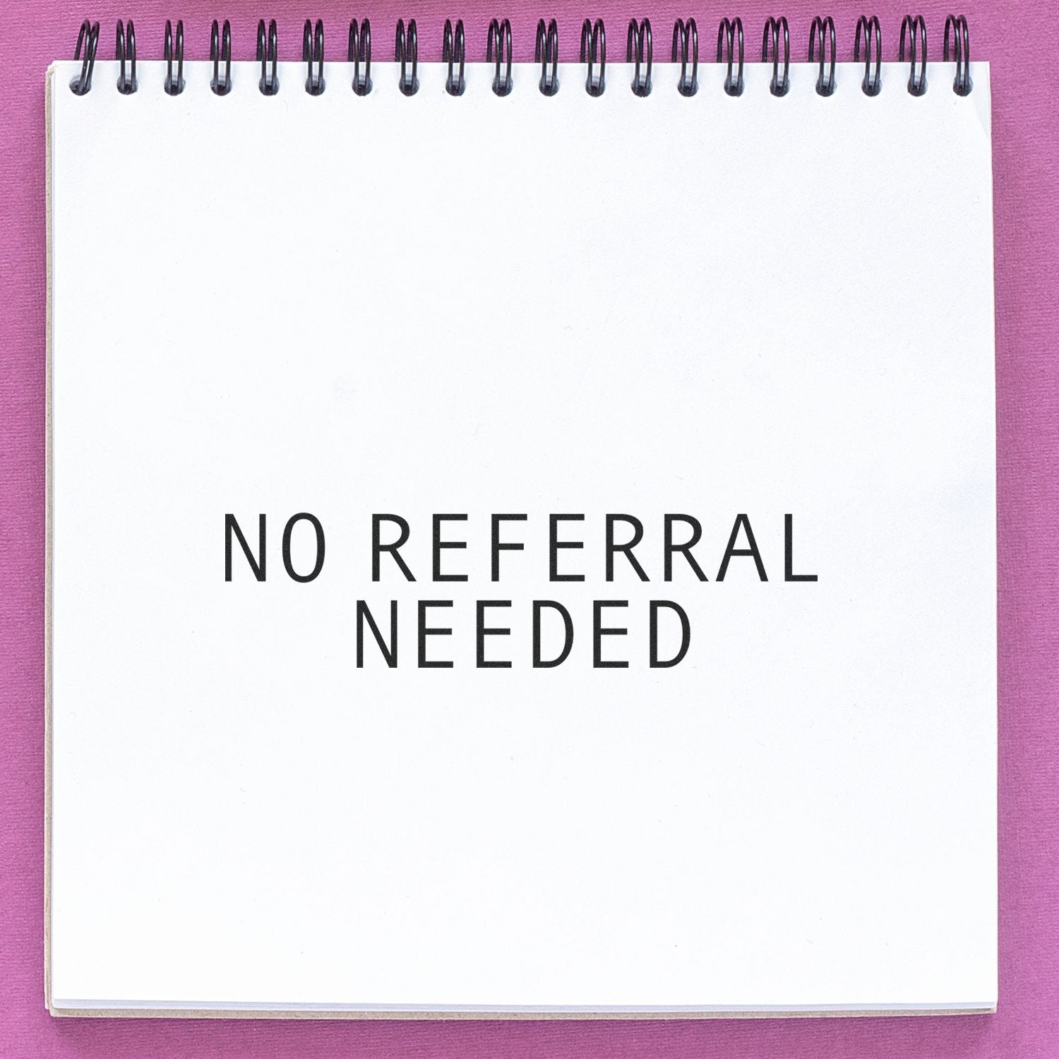 No Referral Needed Medical Rubber Stamp impression on a white spiral notebook, placed on a pink surface.