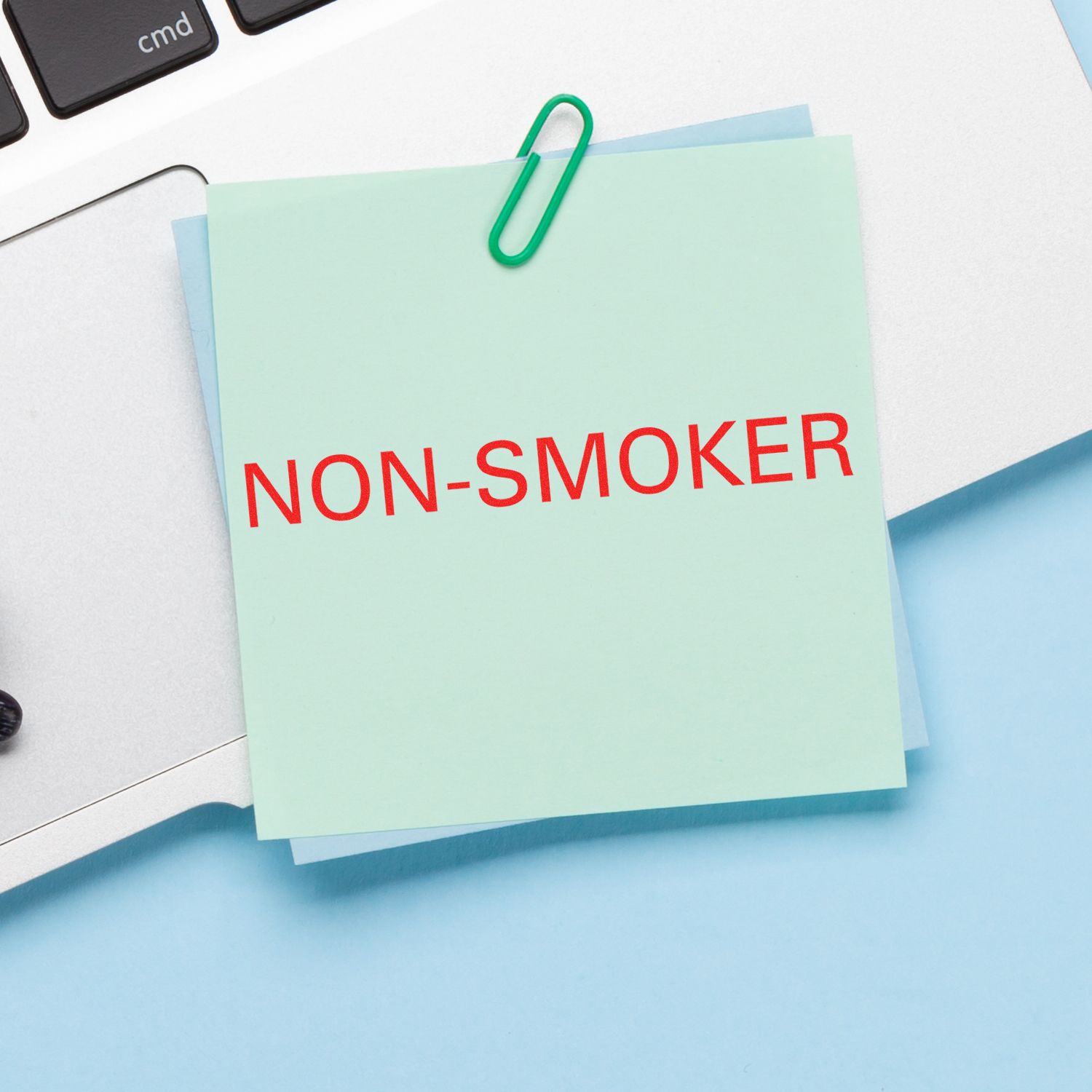 Slim Pre-Inked Non-Smoker Stamp used on a green sticky note clipped to a laptop, displaying NON-SMOKER in red text.