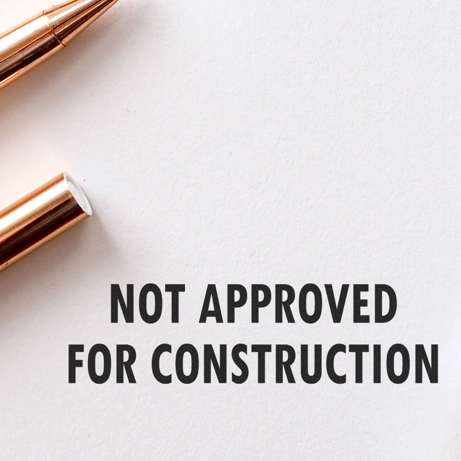 Large Not Approved For Construction Rubber Stamp imprint on white paper, with a gold pen nearby.