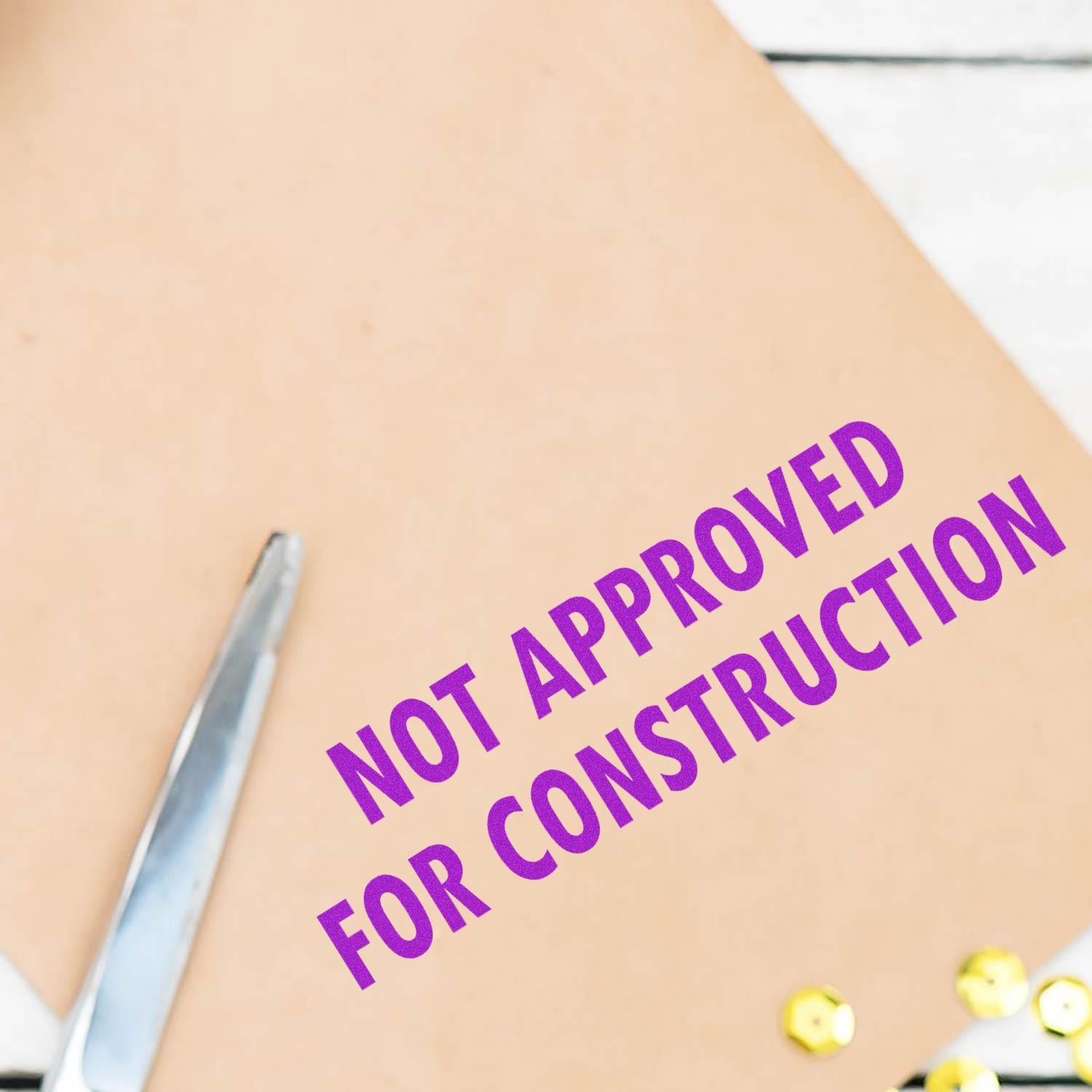 Large Not Approved For Construction Rubber Stamp in use, stamping NOT APPROVED FOR CONSTRUCTION in purple on a beige document