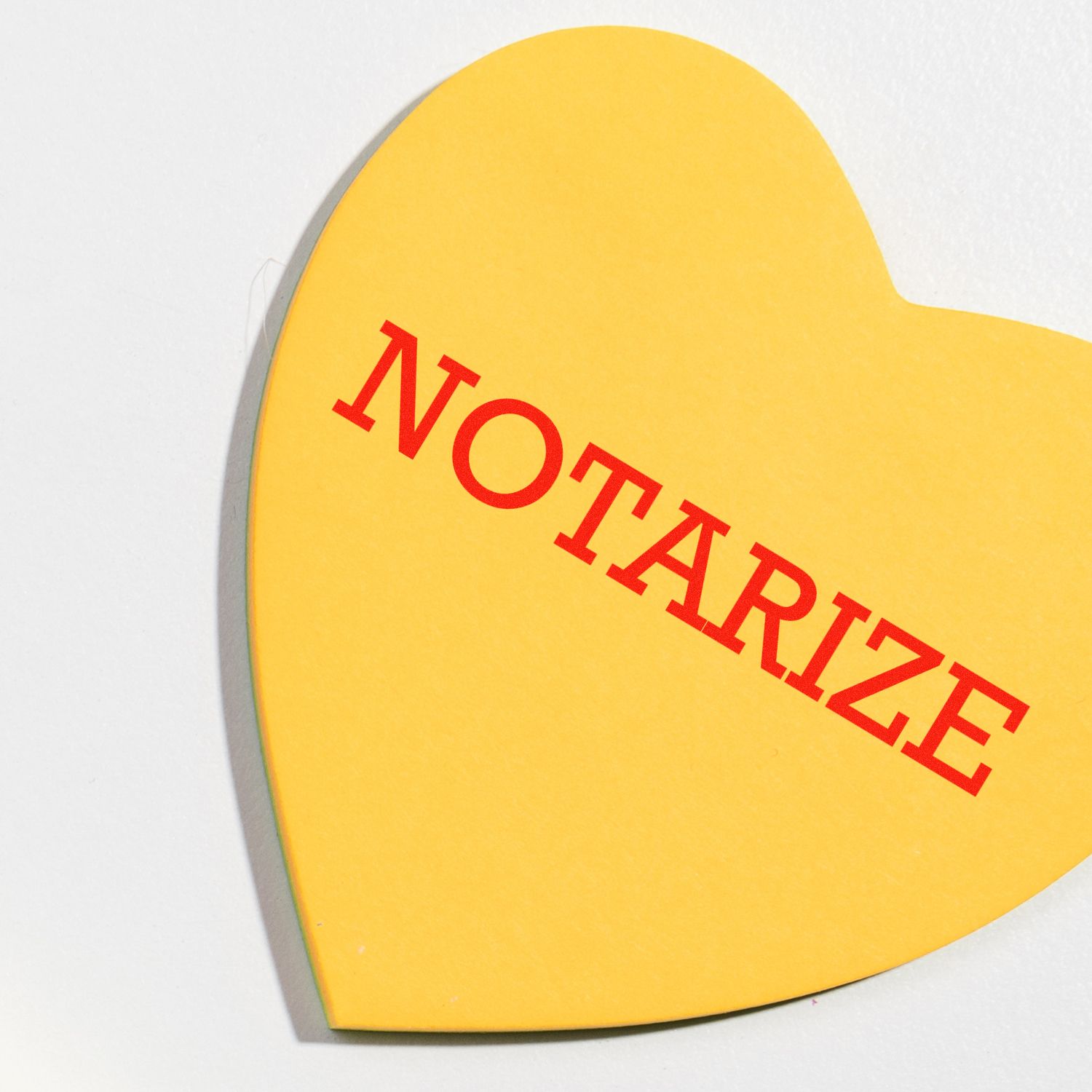 Yellow heart-shaped paper with NOTARIZE stamped in red using a Self Inking Notarize Stamp, placed on a white surface.