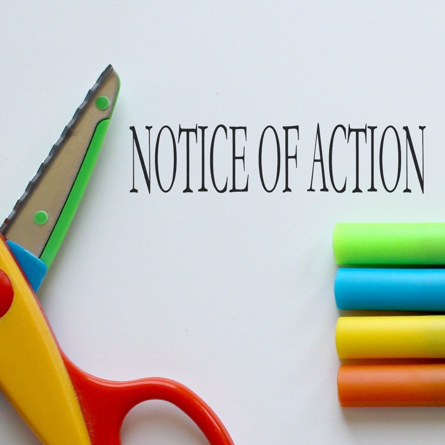 Large Pre-Inked Notice Of Action Stamp in use on white paper, with colorful scissors and markers nearby.