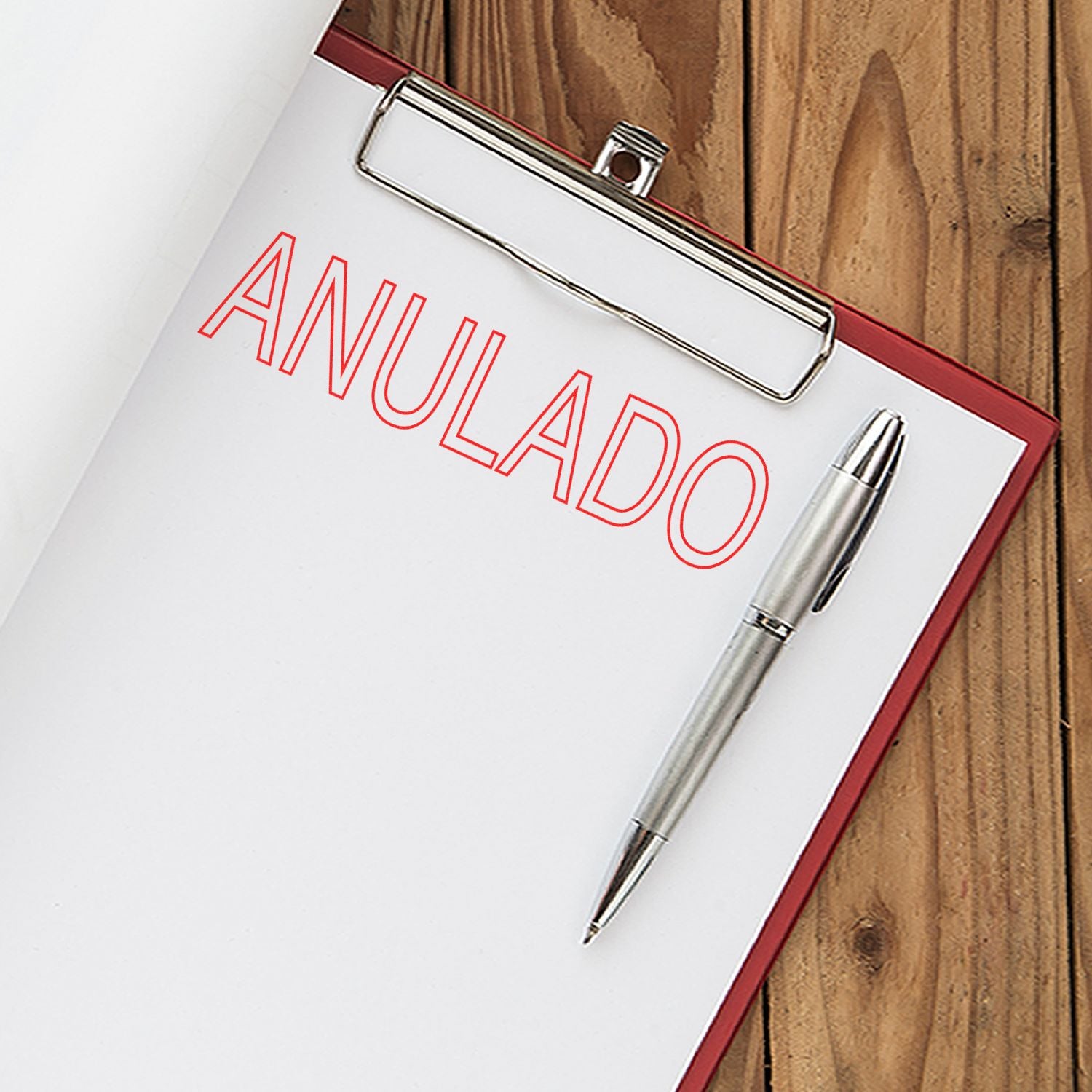 Clipboard with a sheet stamped ANULADO in red using an Outline Anulado Rubber Stamp, next to a silver pen on a wooden surface.