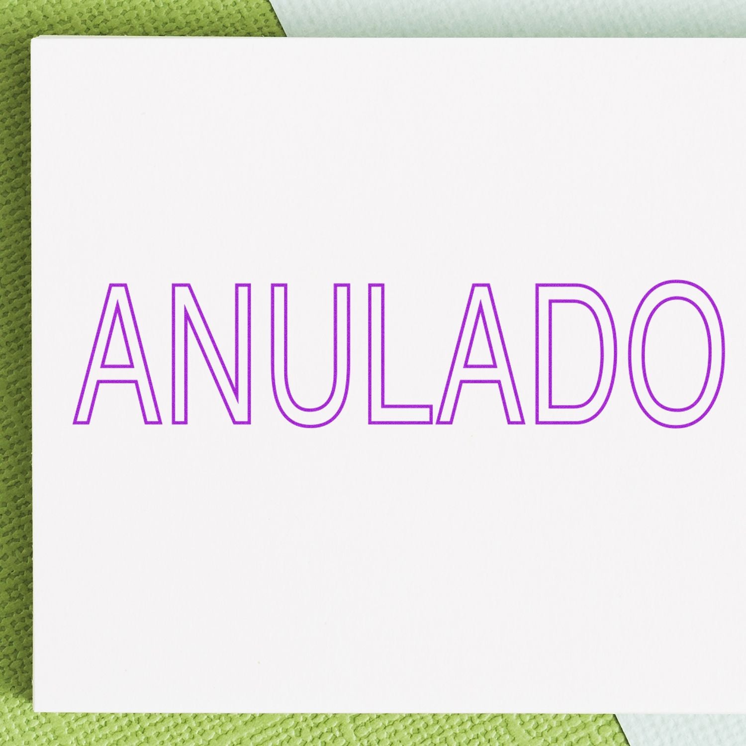 Outline Anulado Rubber Stamp in purple ink on white paper, placed on a textured green and white background.