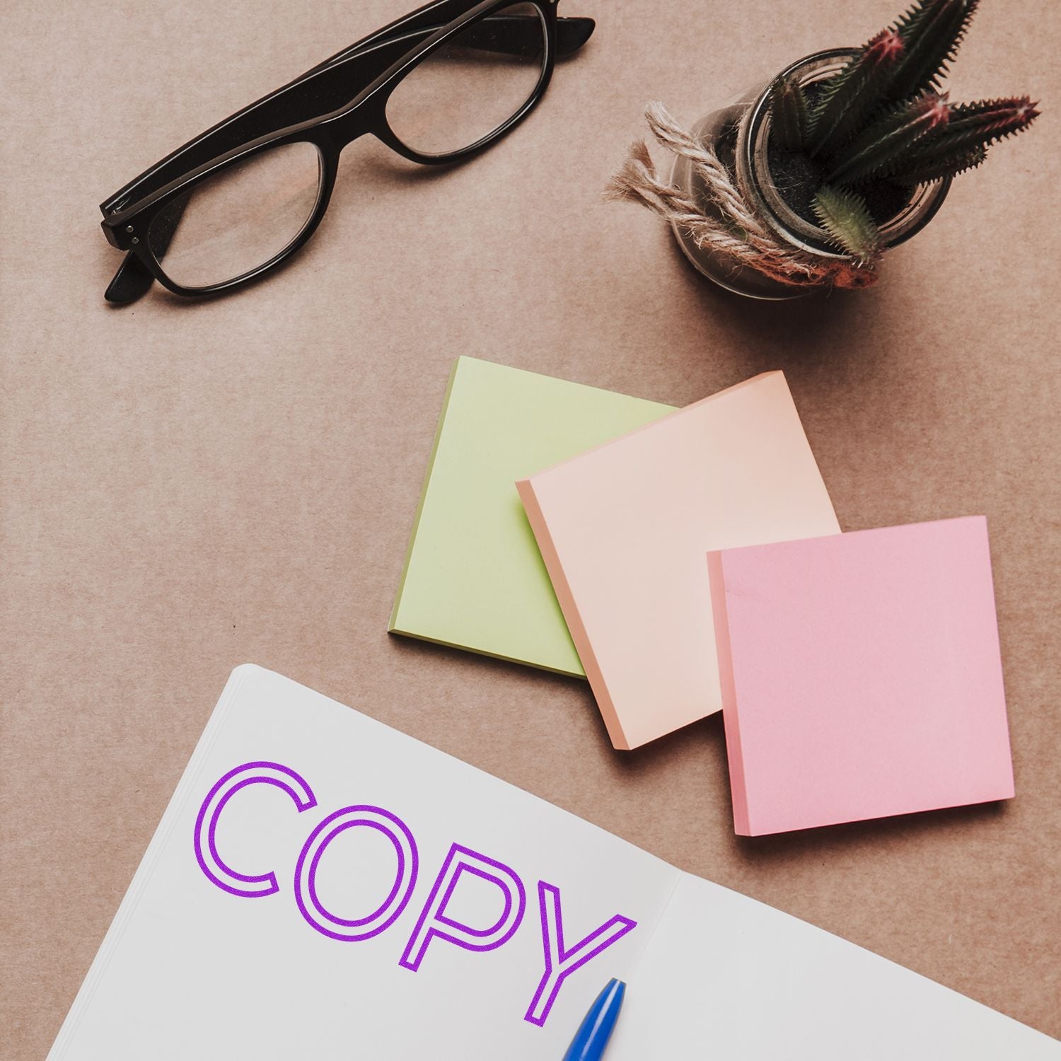 Large Self Inking Outline Copy Stamp in use on a notebook with COPY stamped, surrounded by sticky notes, glasses, and a potted plant.