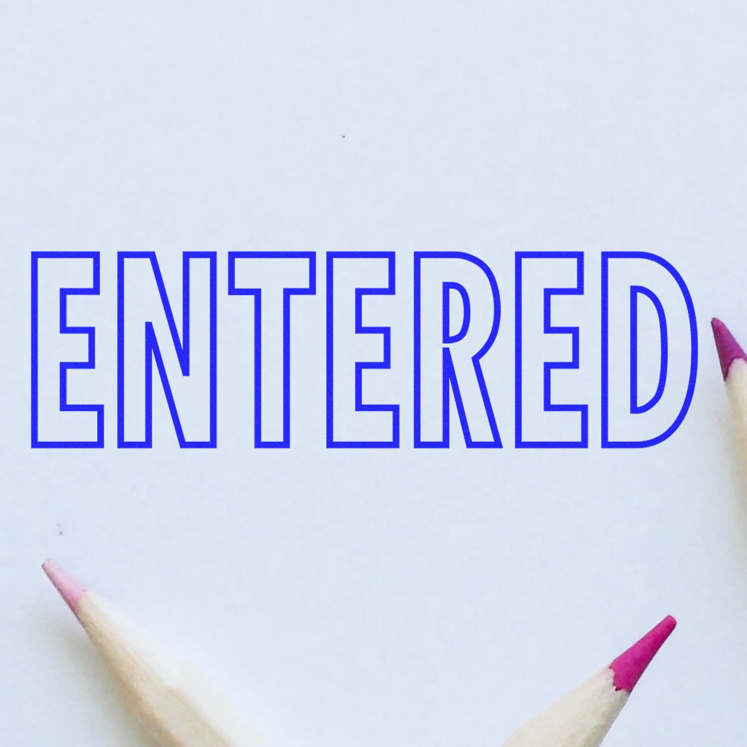 Outline Entered Rubber Stamp in blue ink on white paper, surrounded by three sharpened pencils with pink tips.