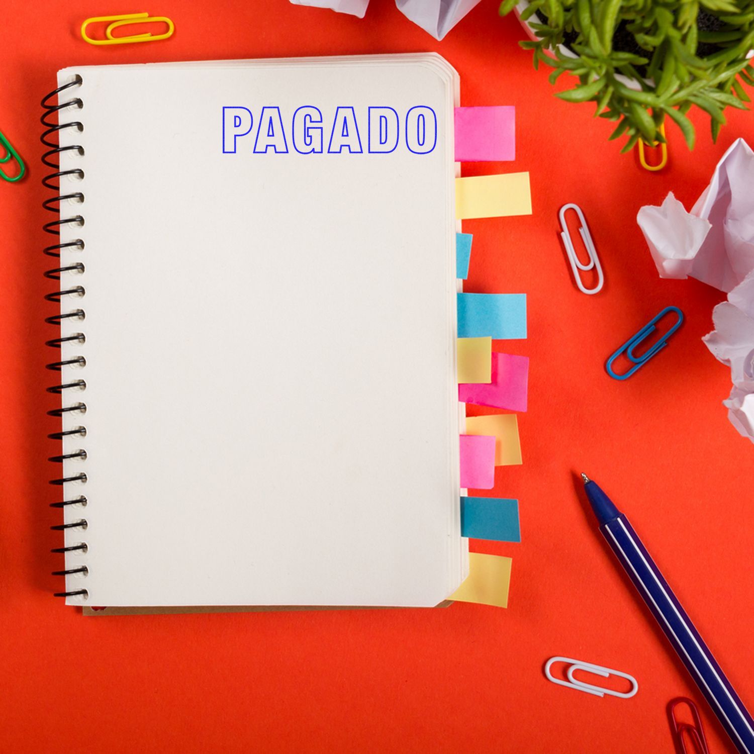 Large Pre-Inked Outline Pagado Stamp used on a spiral notebook with colorful sticky tabs, paper clips, and a pen on a red background.