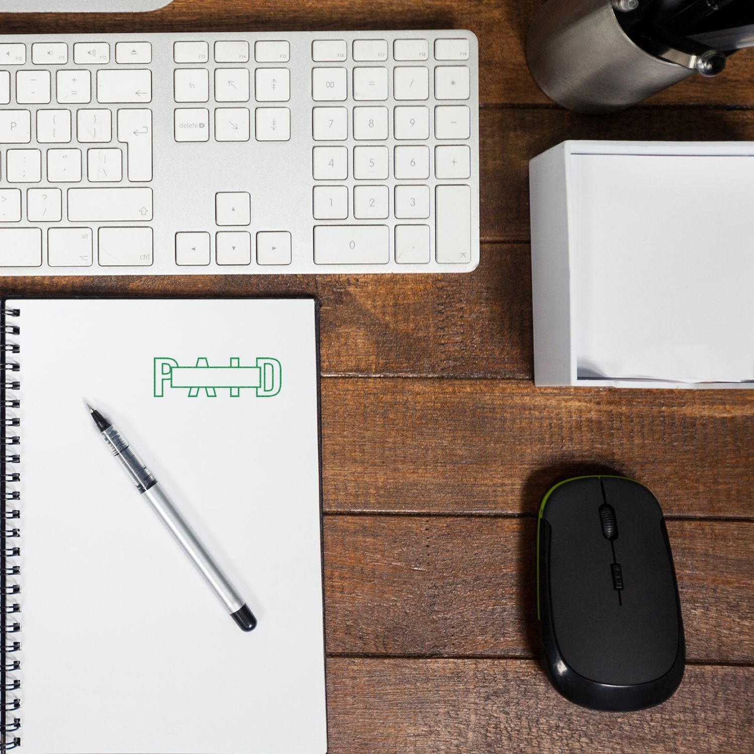 Large Self Inking Outline Paid with Box Stamp on a notebook beside a pen, keyboard, mouse, and a box on a wooden desk.