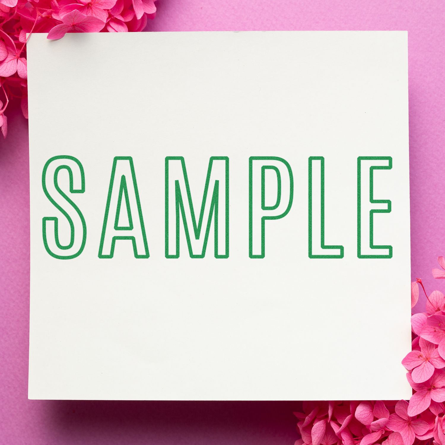 Outline Sample Rubber Stamp impression on white paper with green ink, surrounded by pink flowers on a pink background.