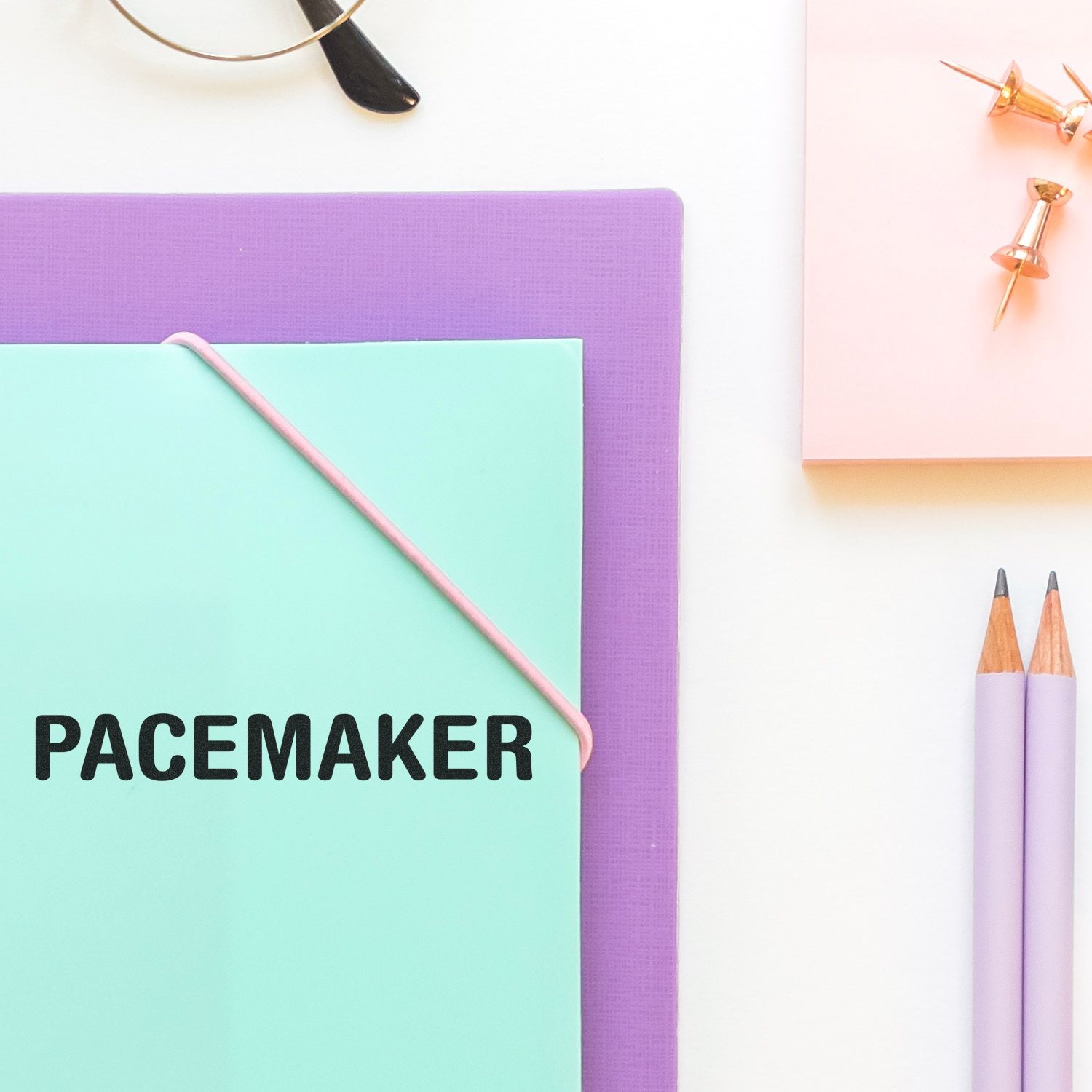 Slim Pre-Inked Pacemaker Stamp on a mint green folder, surrounded by purple and pink stationery items on a white desk.