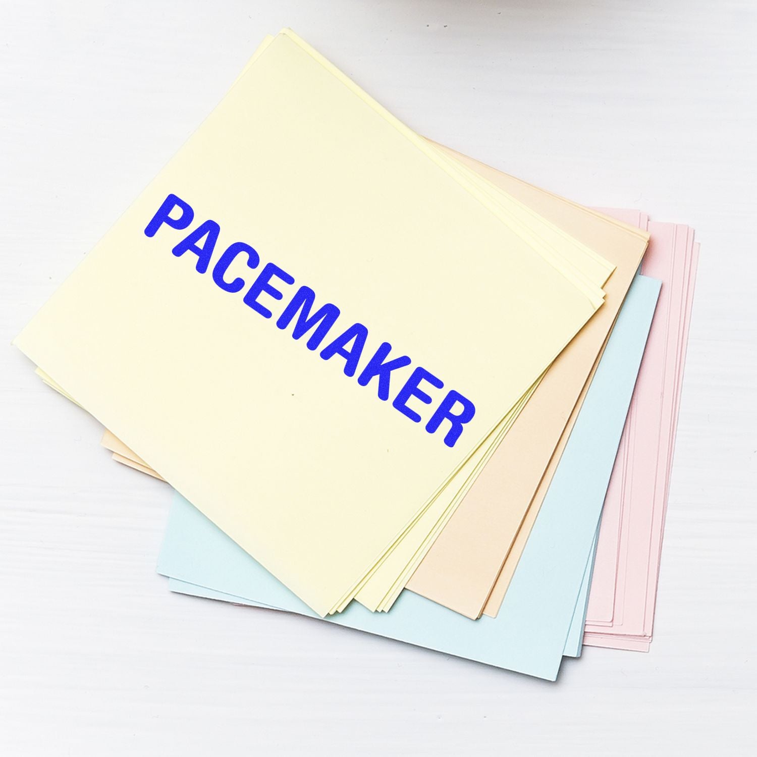 Pacemaker rubber stamp impression on a stack of pastel-colored papers, showcasing the bold blue text PACEMAKER on top.