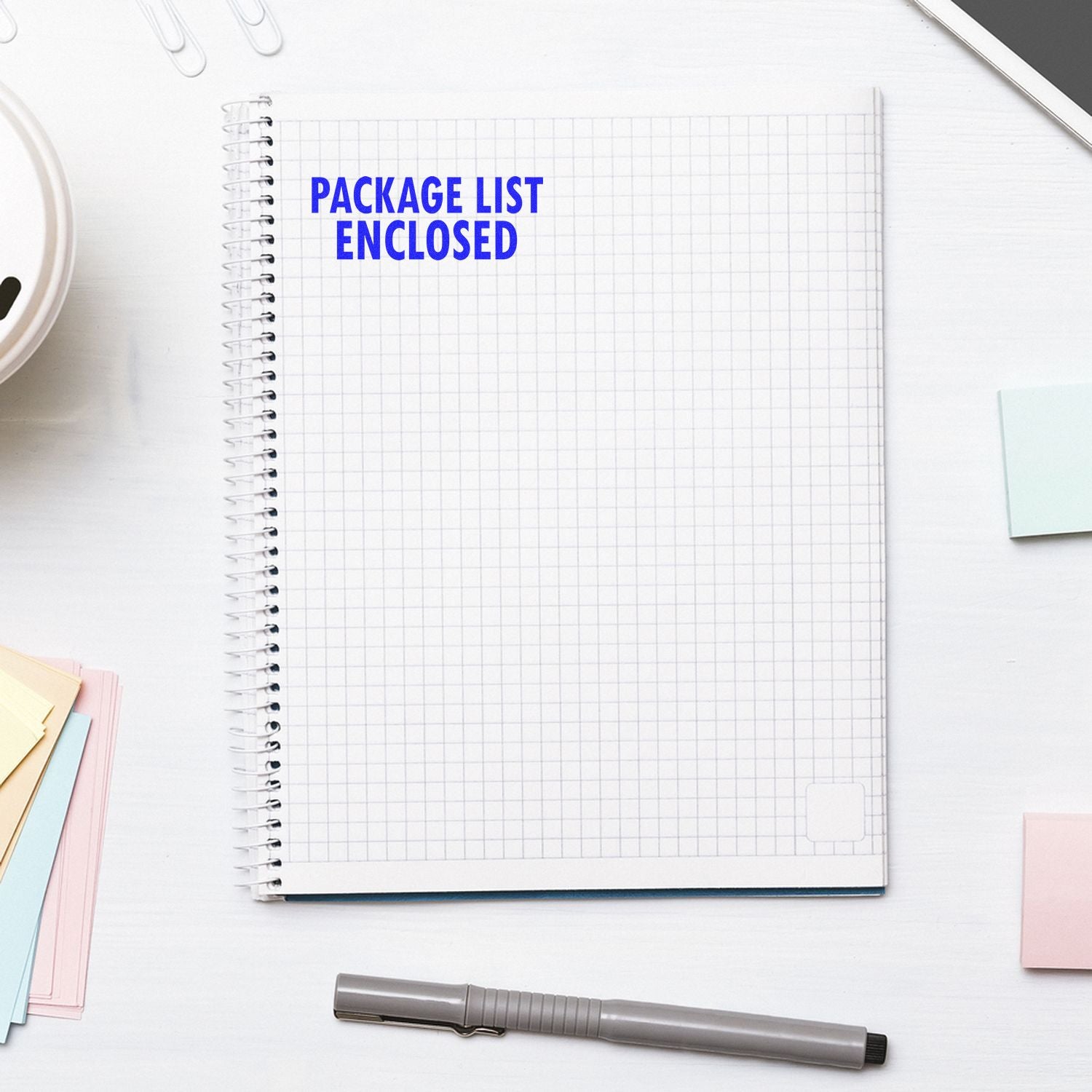 Notebook with a Package List Enclosed rubber stamp impression on the top left, surrounded by office supplies on a white desk.