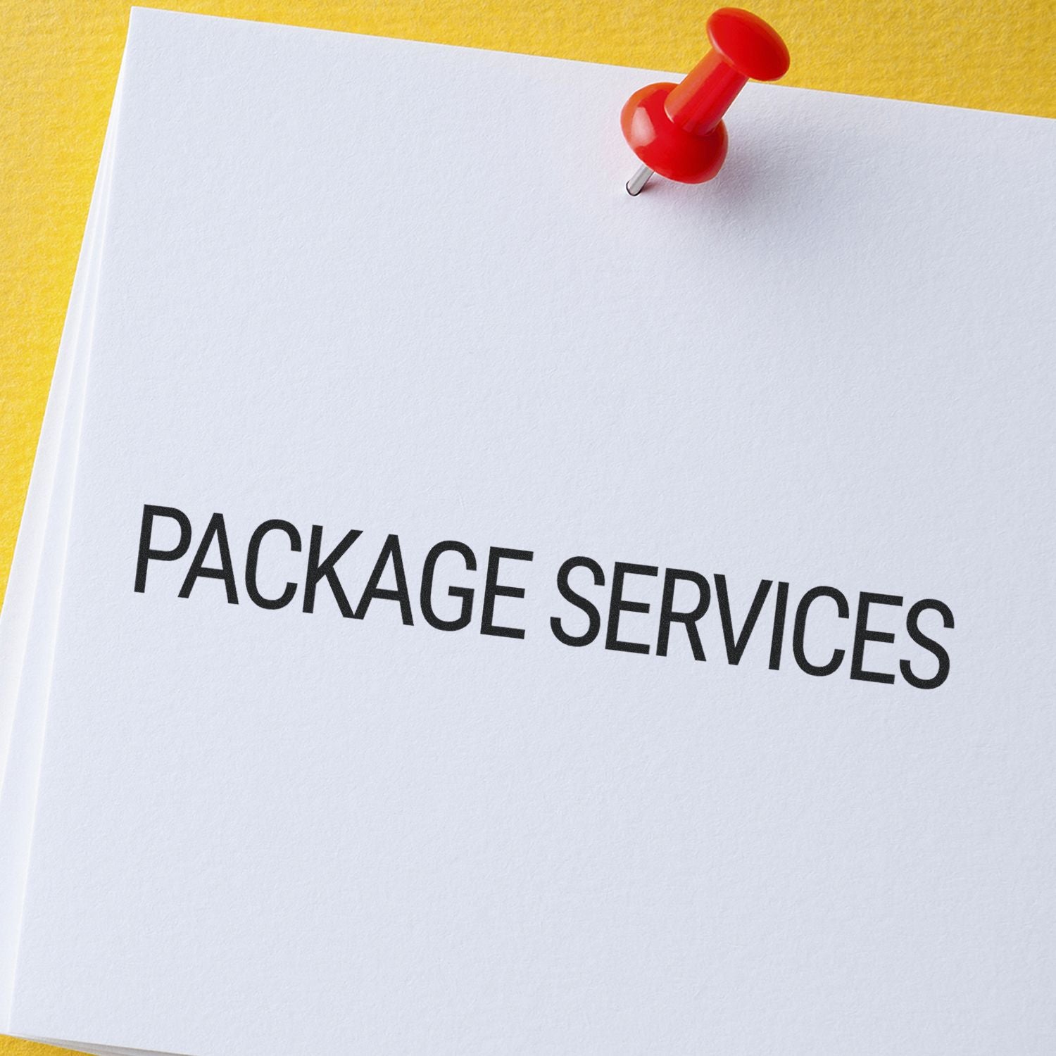 A red pushpin holds a white paper with PACKAGE SERVICES stamped on it using the Large Package Services Rubber Stamp, against a yellow background.