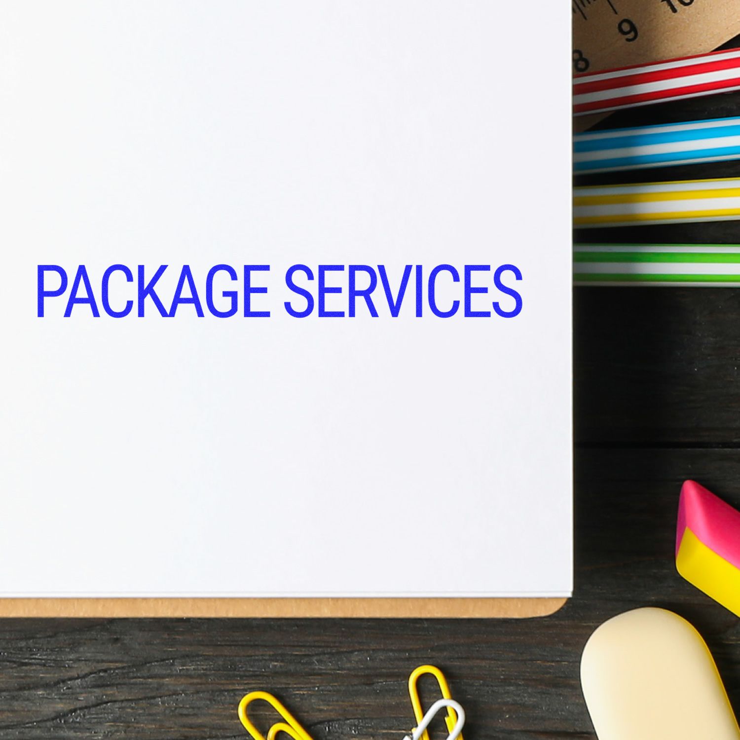 Package Services rubber stamp on white paper, surrounded by colorful paper clips and a ruler on a dark wooden desk.