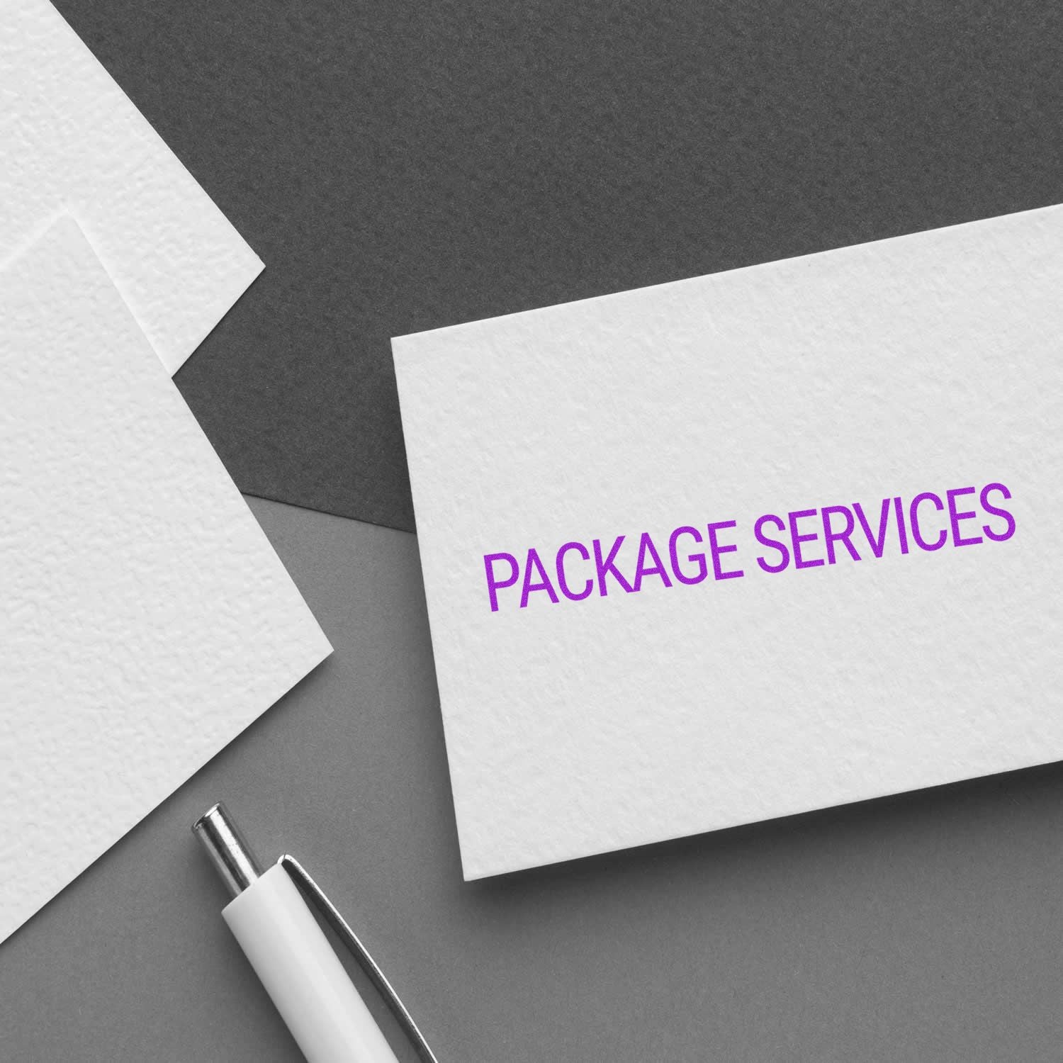 Package Services rubber stamp on a white card, placed on a gray surface with a pen and additional cards nearby.