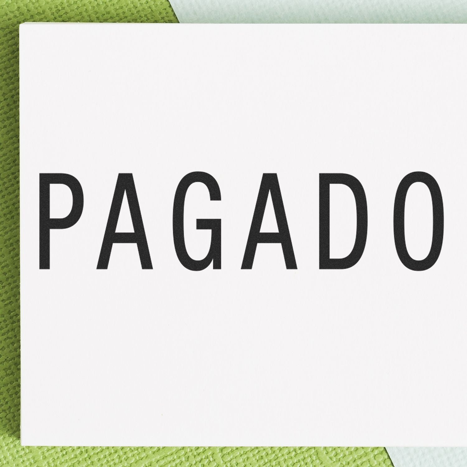 Close-up of a white card with the word 'PAGADO' stamped in bold black letters using a Pagado rubber stamp, on a green background.