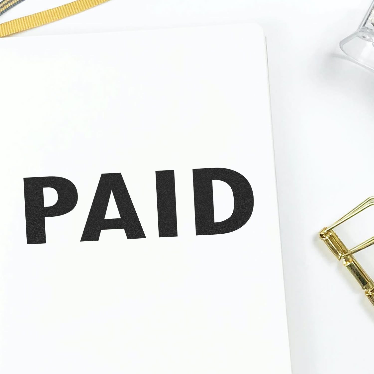 Large Self Inking Paid Stamp marking PAID in bold black letters on a white paper, with a gold paperclip and clear stamp holder nearby.