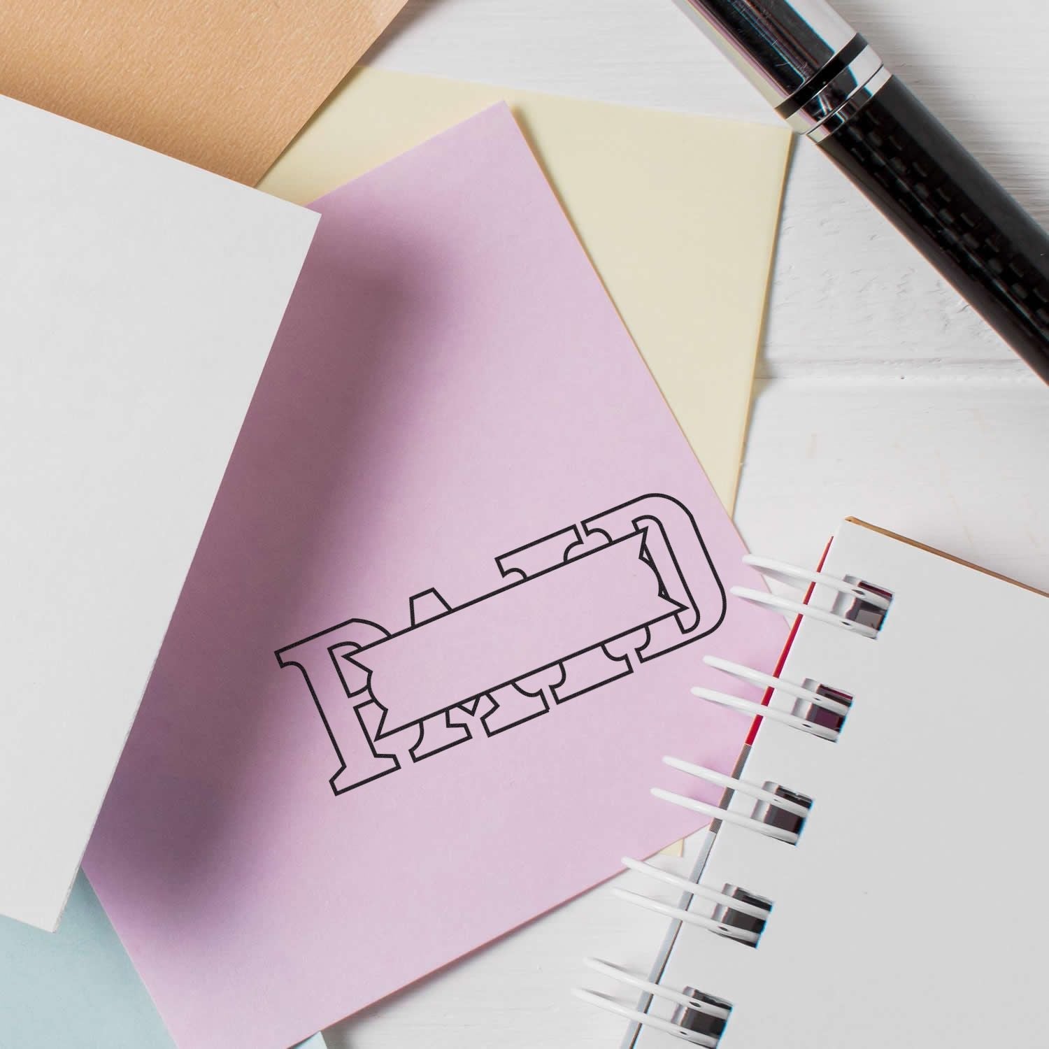 Self Inking Paid with Box Stamp marking PAID on a pink paper, surrounded by other papers and a pen on a white desk.