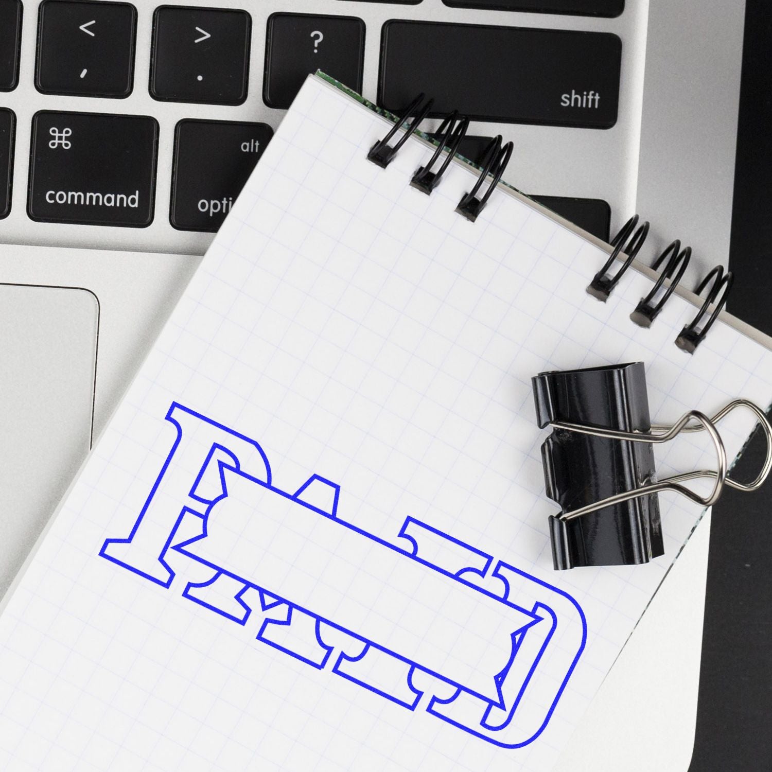 Large Self Inking Paid with Box Stamp used on a notepad placed on a laptop keyboard, with a black binder clip attached to the notepad.