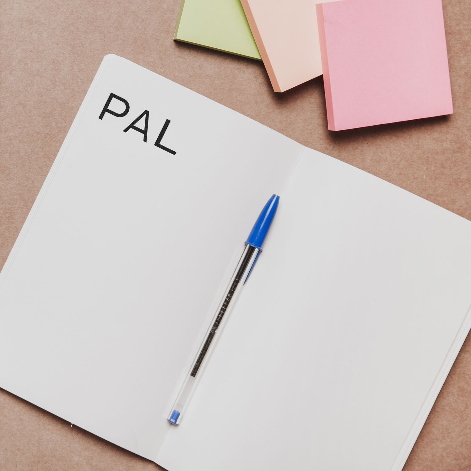 Large PAL Rubber Stamp used on an open notebook with a blue pen and colorful sticky notes in the background.