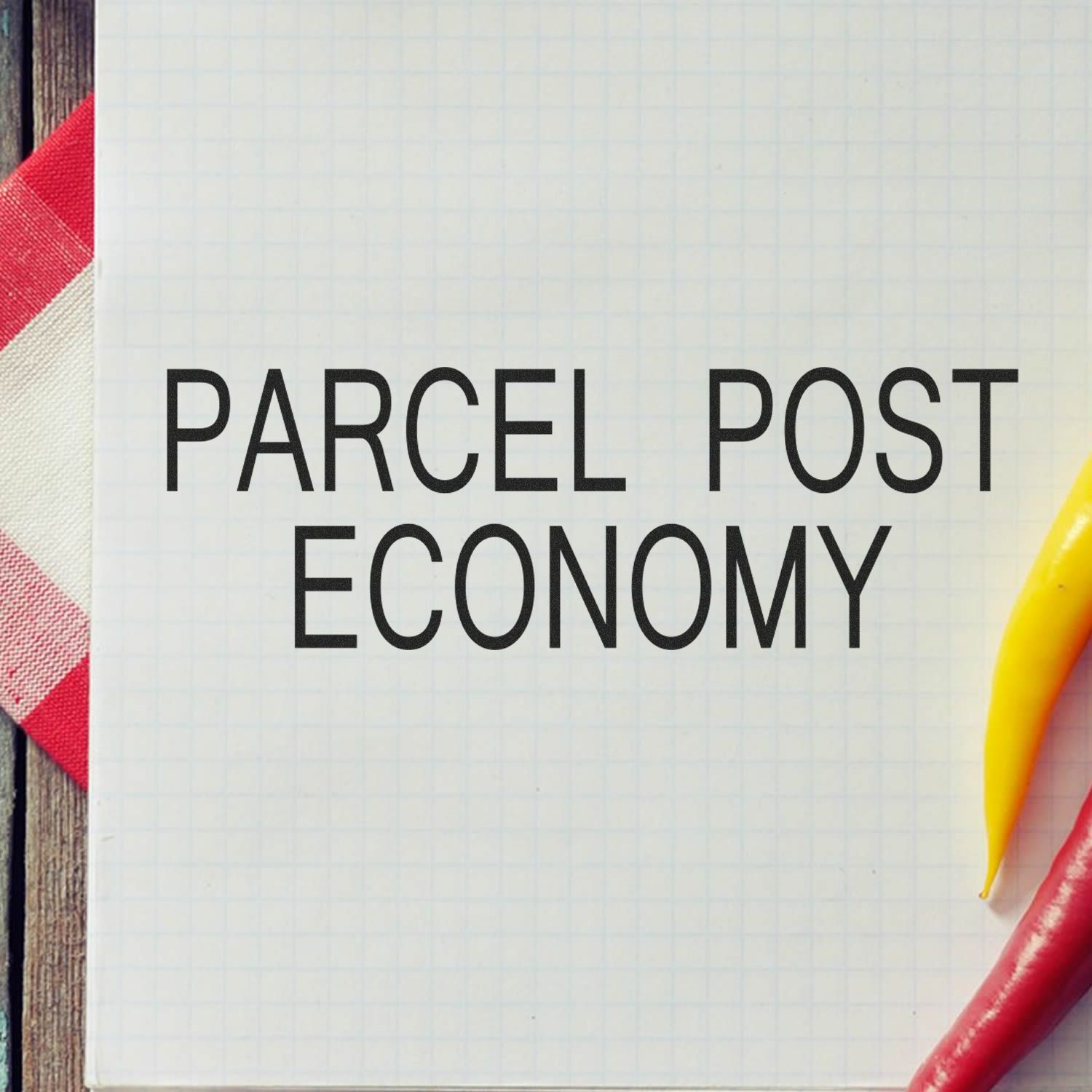 Large Parcel Post Economy Rubber Stamp used on a white grid paper, with a red and white cloth and yellow and red chili peppers nearby.