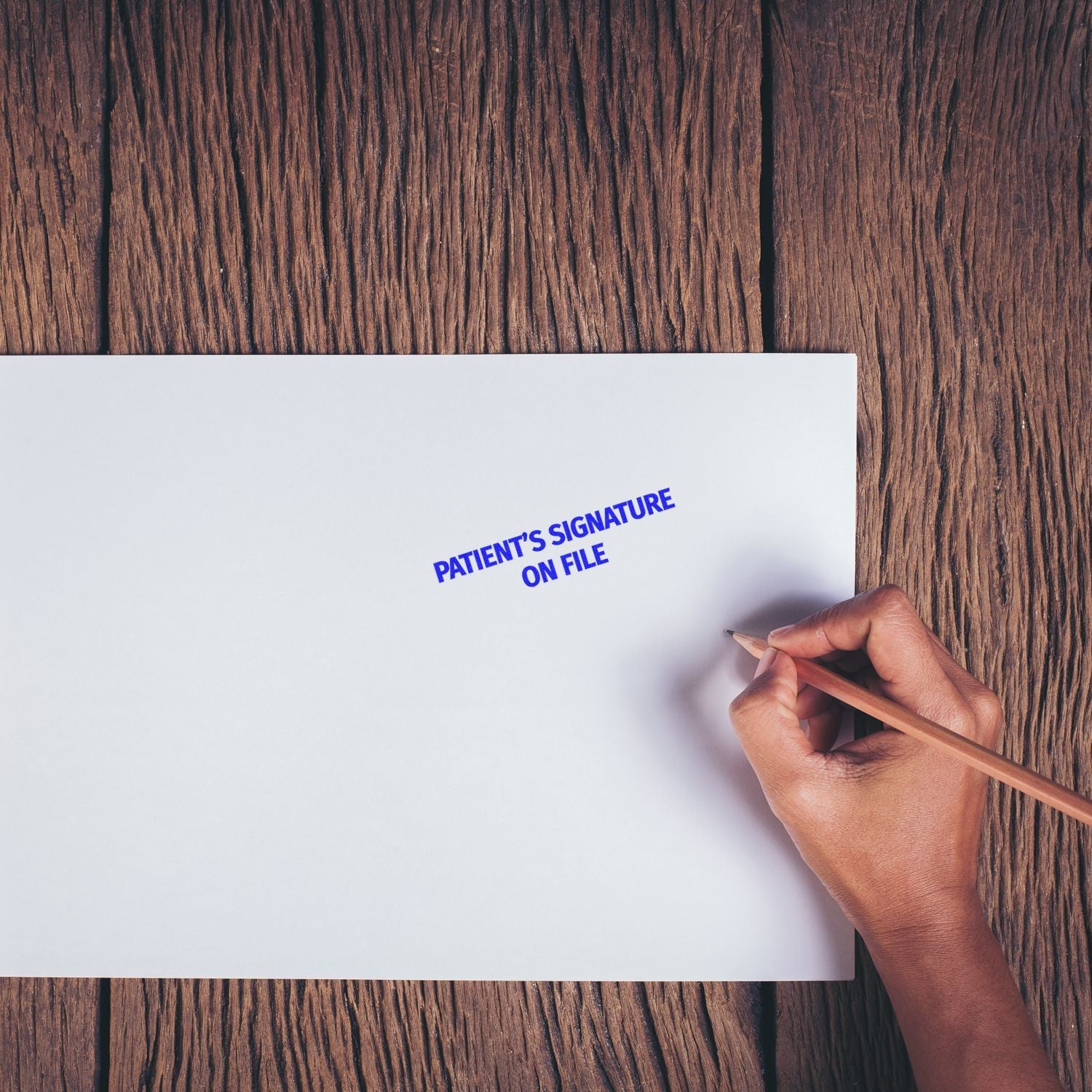 Hand using the Self Inking Patient's Signature on File Stamp on a white paper against a wooden background.