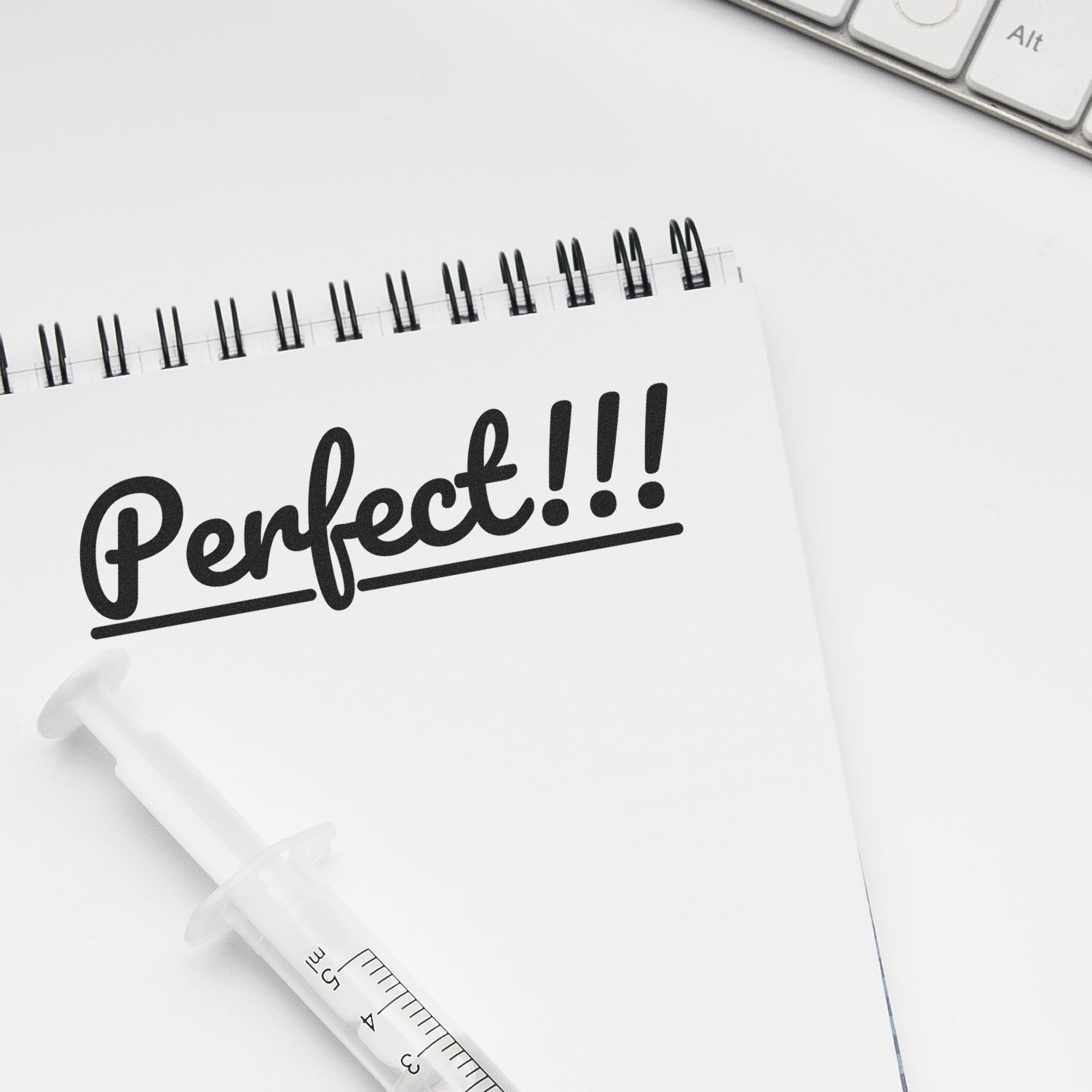 A Large Self Inking Perfect Stamp imprinting the word Perfect!!! on a spiral notebook, with a syringe and keyboard nearby.