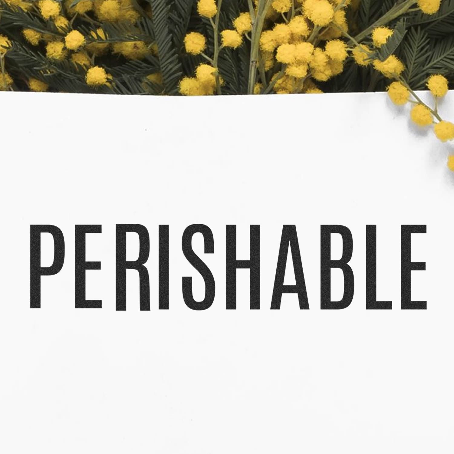 Perishable Rubber Stamp in use, stamping the word "PERISHABLE" on white paper, with yellow flowers in the background.