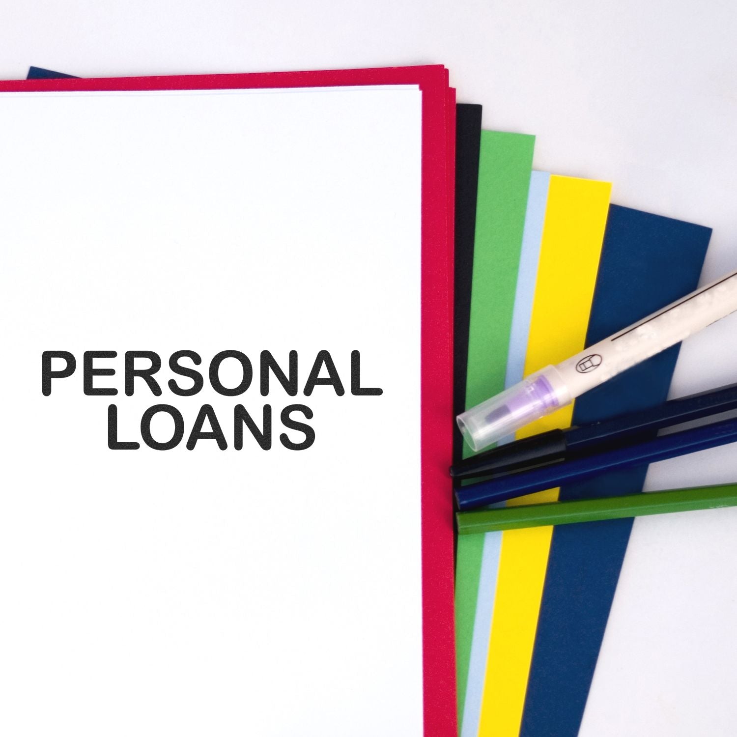 Personal Loans rubber stamp on white paper with colorful sheets and pens in the background.