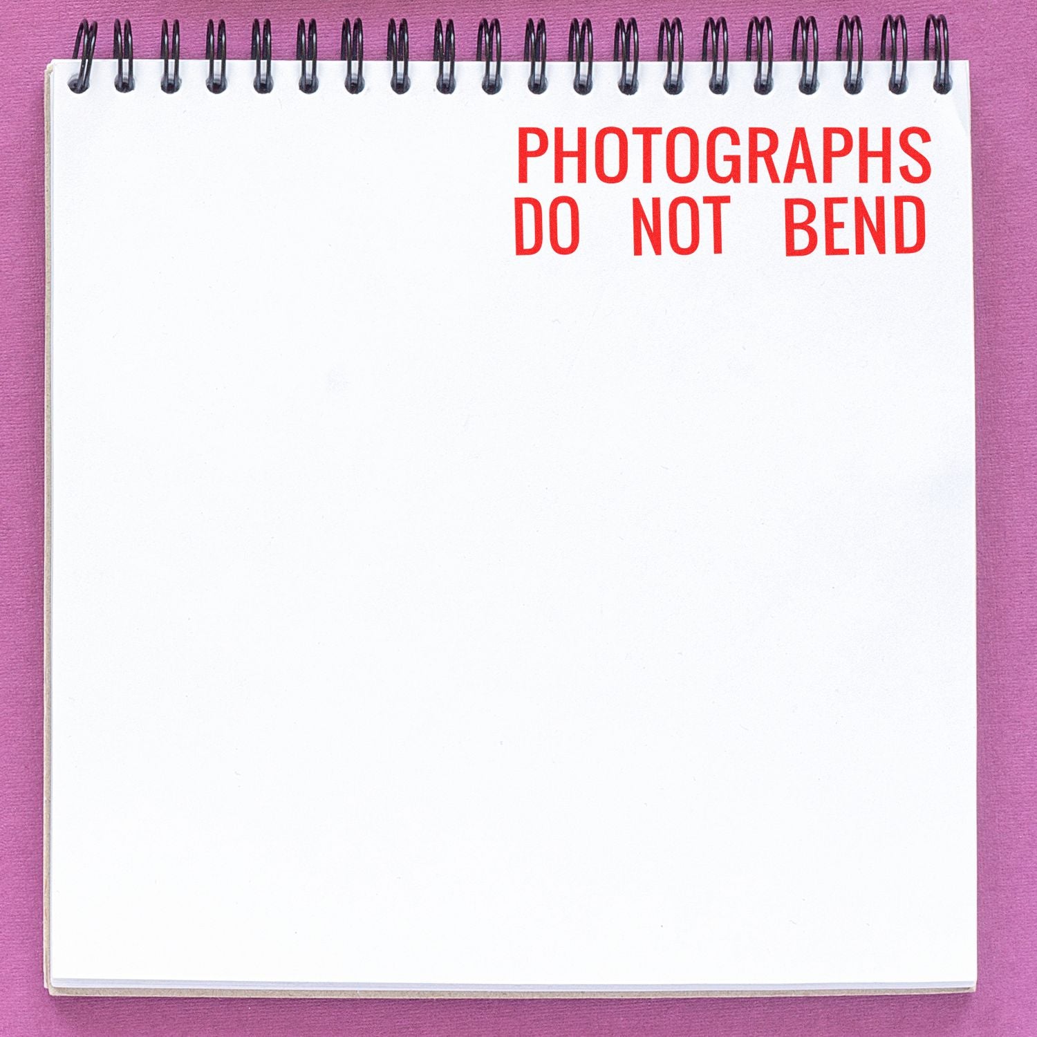 Photographs Do Not Bend rubber stamp in red ink on a white spiral notebook against a purple background.