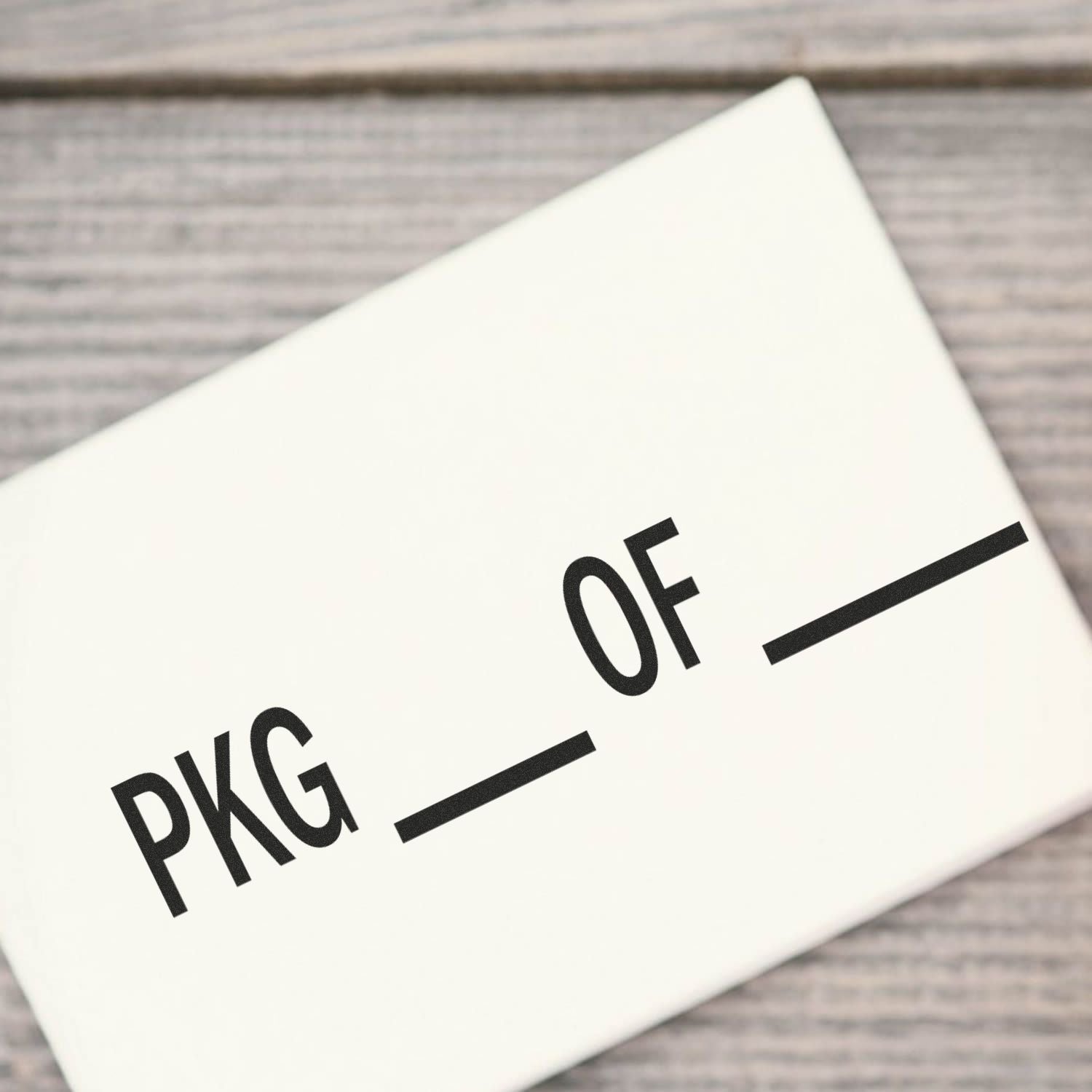 Slim Pre-Inked Pkg Of Stamp in use, showing the text "PKG ___ OF ___" stamped on a white surface against a wooden background.