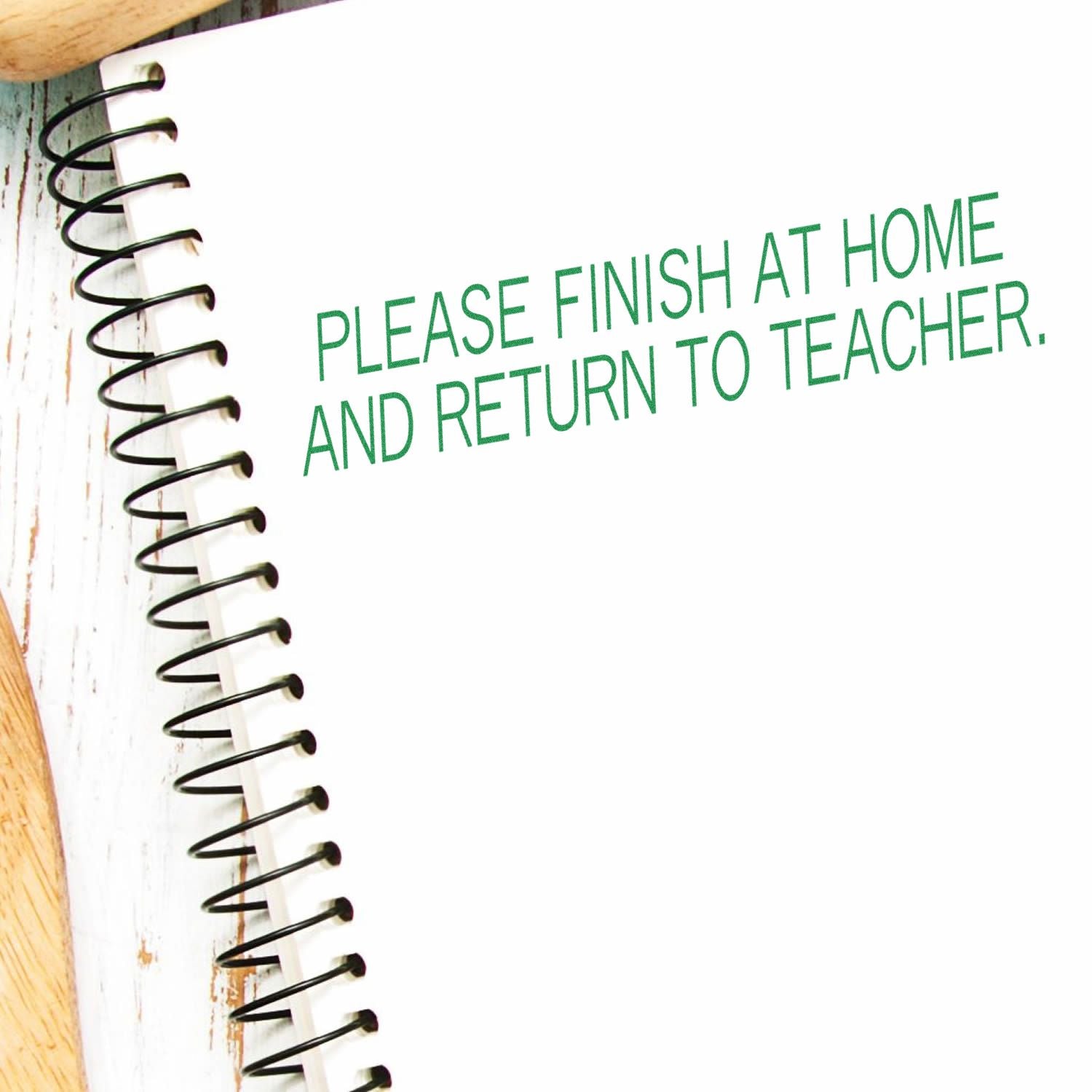 A notebook with a Please Finish At Home Return To Teacher rubber stamp message in green ink on a white page.