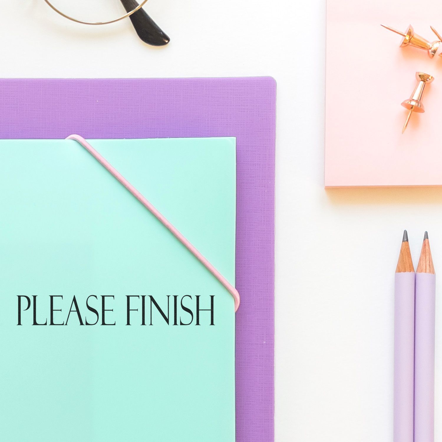 Large Self Inking Please Finish Stamp used on a mint green folder, placed on a purple mat with pencils, push pins, and glasses nearby.