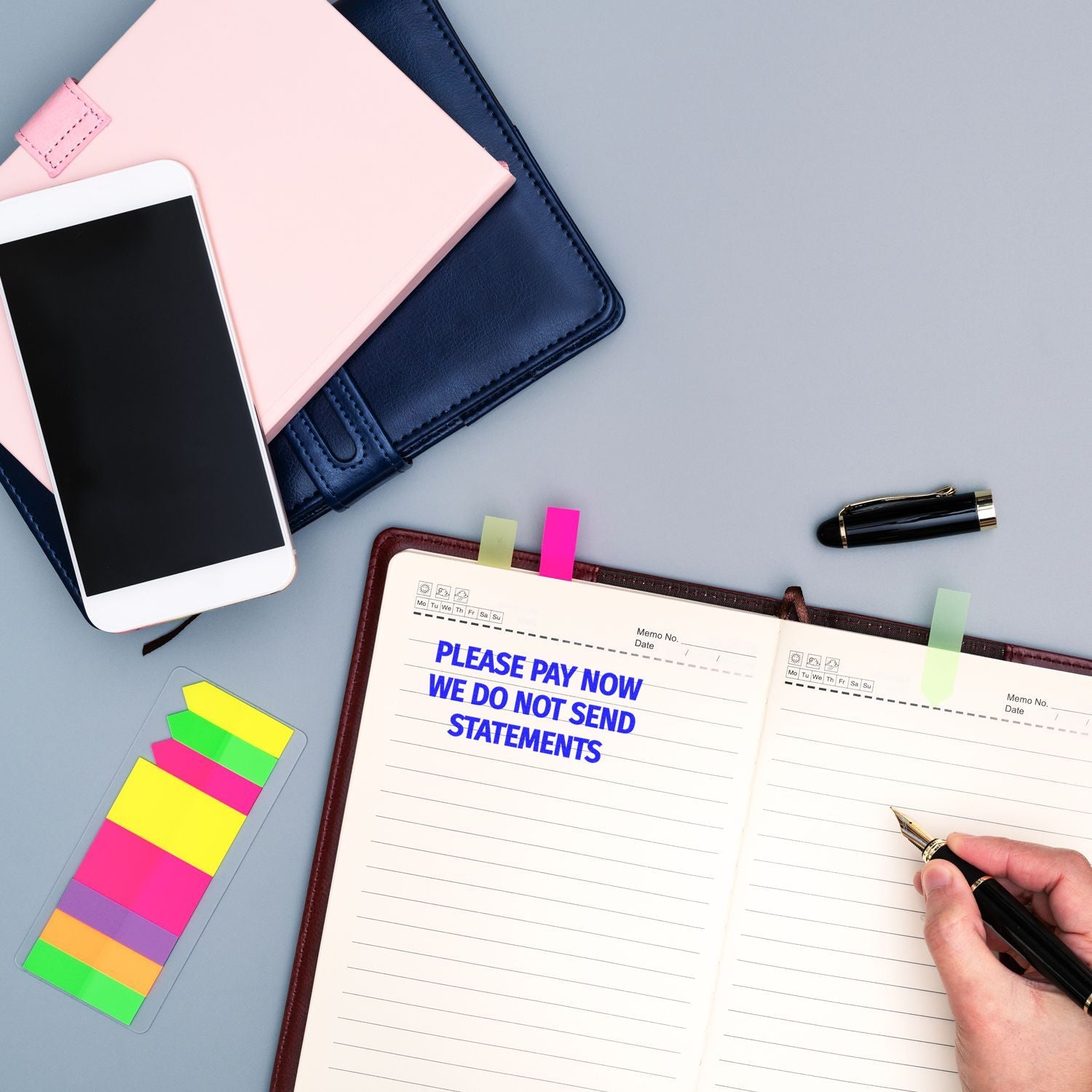 Person writing in a planner with a Please Pay Now No Statements will be Sent rubber stamp impression on the page.