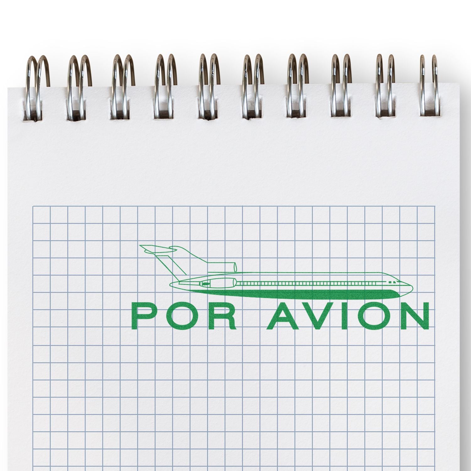 Large Por Avion Rubber Stamp in use on a spiral notebook with grid paper, featuring a green airplane and text POR AVION.